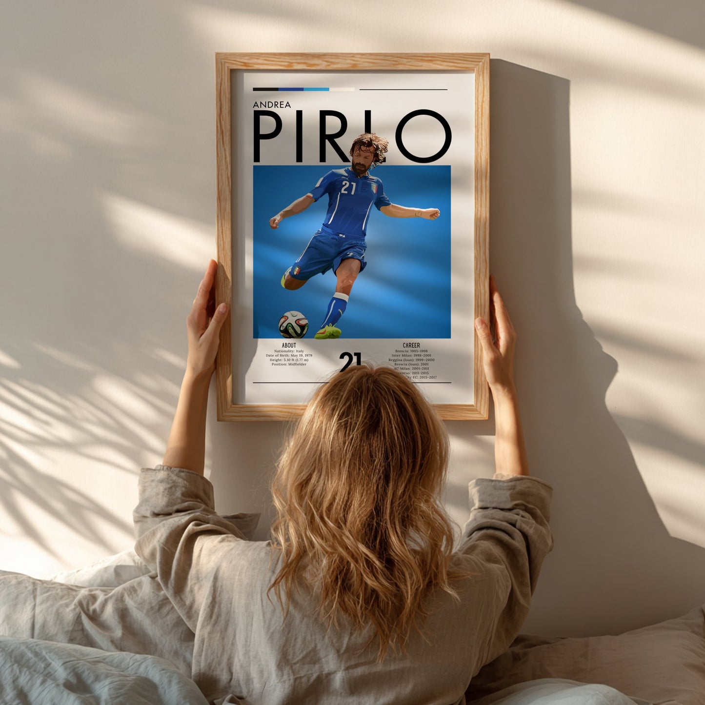 Person hanging a framed poster of Andrea Pirlo on a wall