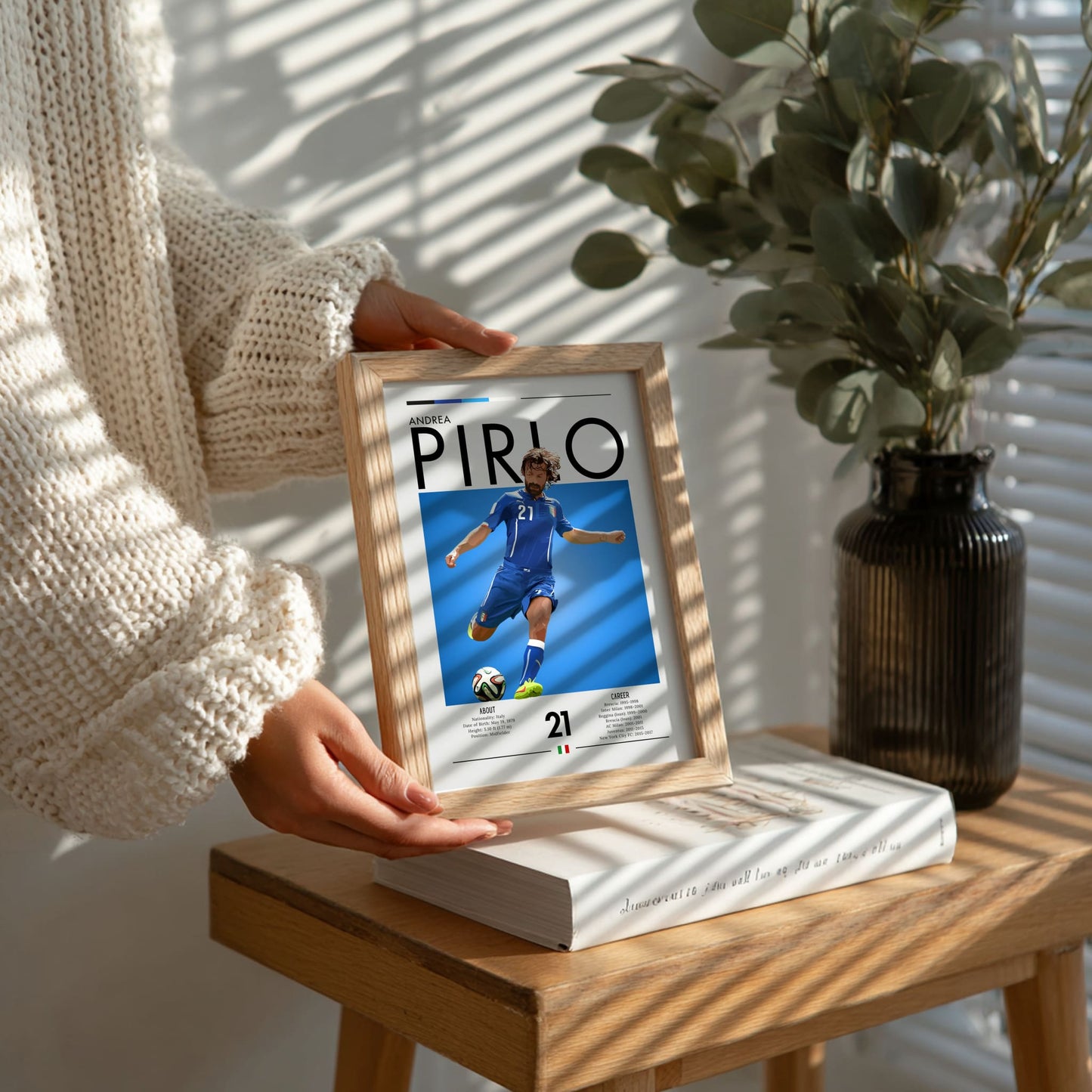 Person holding a framed picture of a soccer player on a wooden table with a plant in the background