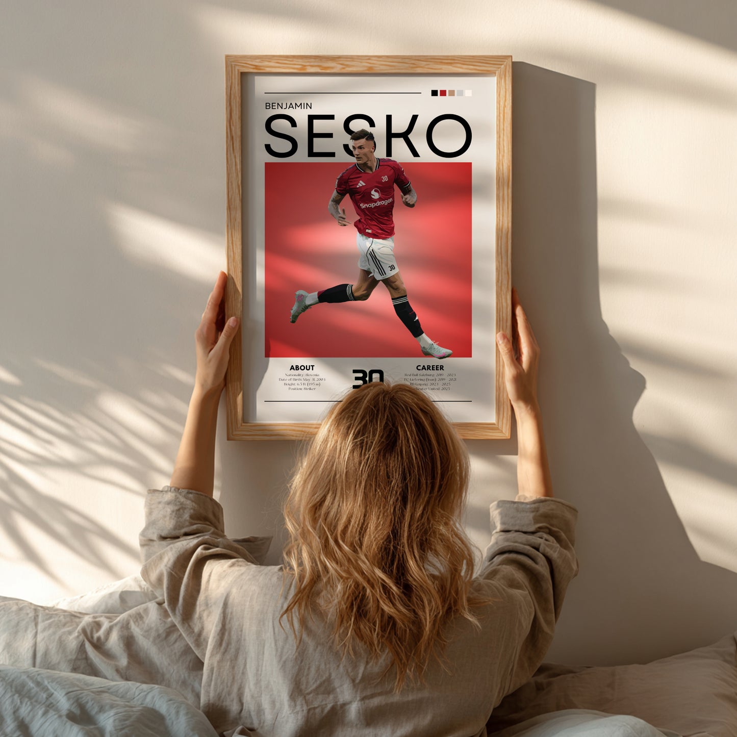 Person hanging a framed poster of a soccer player named 'Sesko' on a wall.