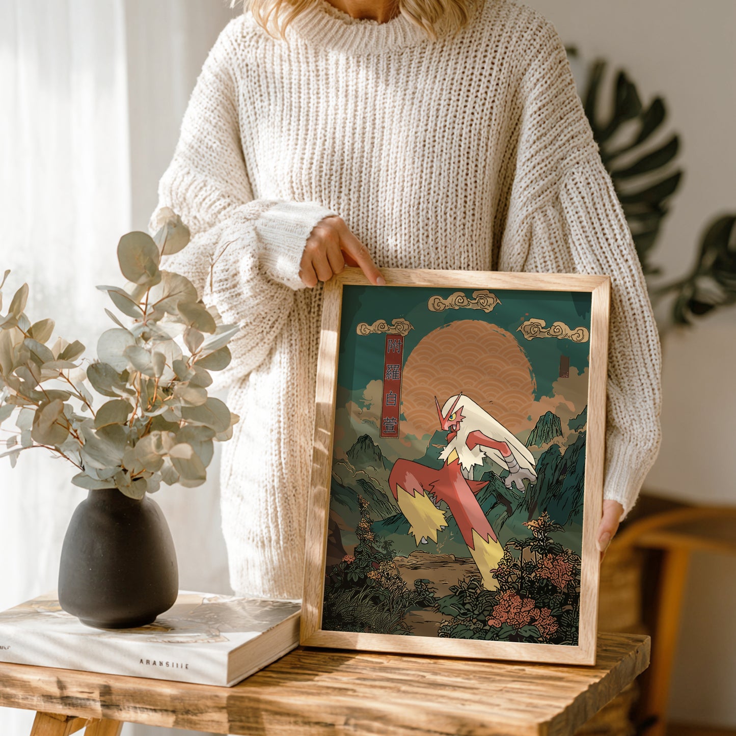 Person holding a framed artwork in a home setting with plants and decor.