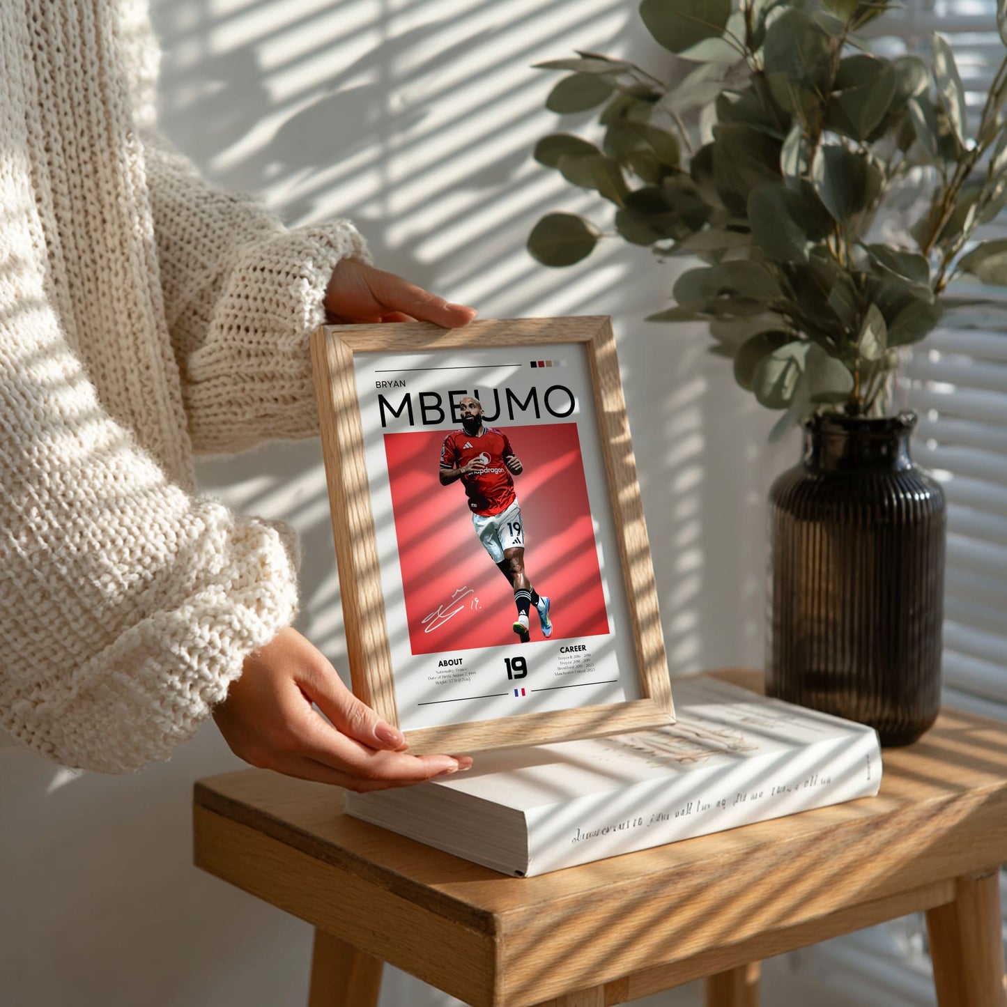 Person holding a framed picture of a sports player on a wooden table with a plant in the background