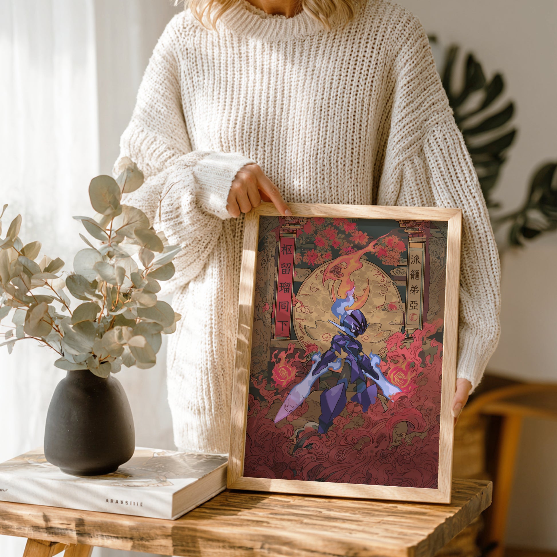 Person holding a framed artwork with Ceruledge Pokemon character in a fantasy setting on a wooden table.
