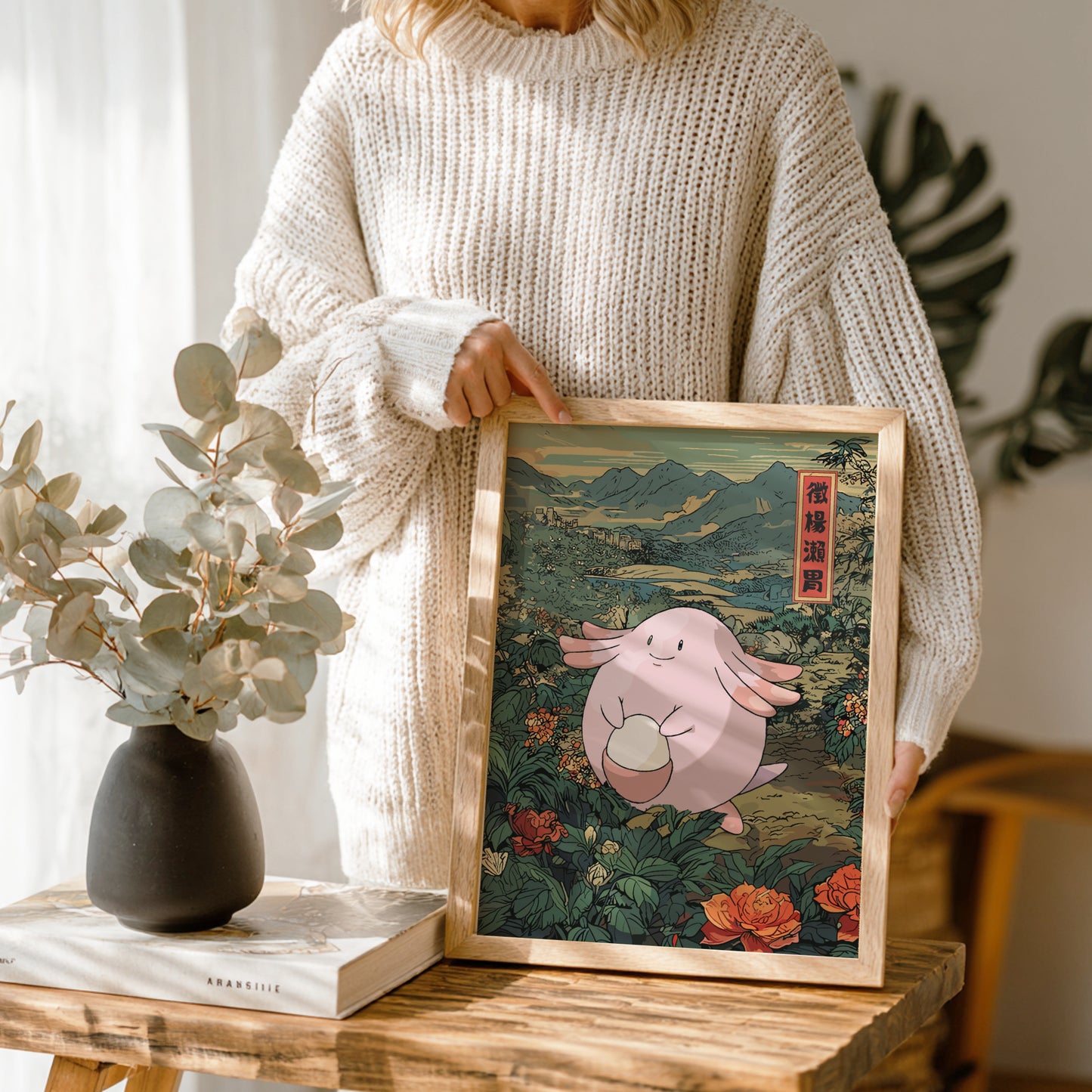 Person holding a framed illustration of Chansey Pokemon in a natural setting