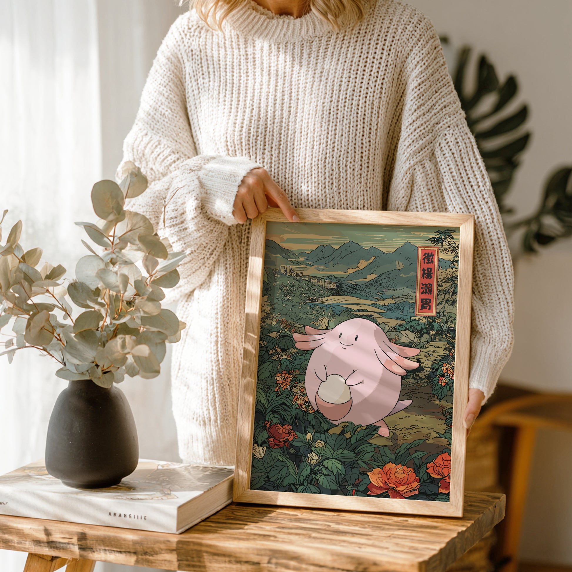 Person holding a framed illustration of Chansey Pokemon in a natural setting