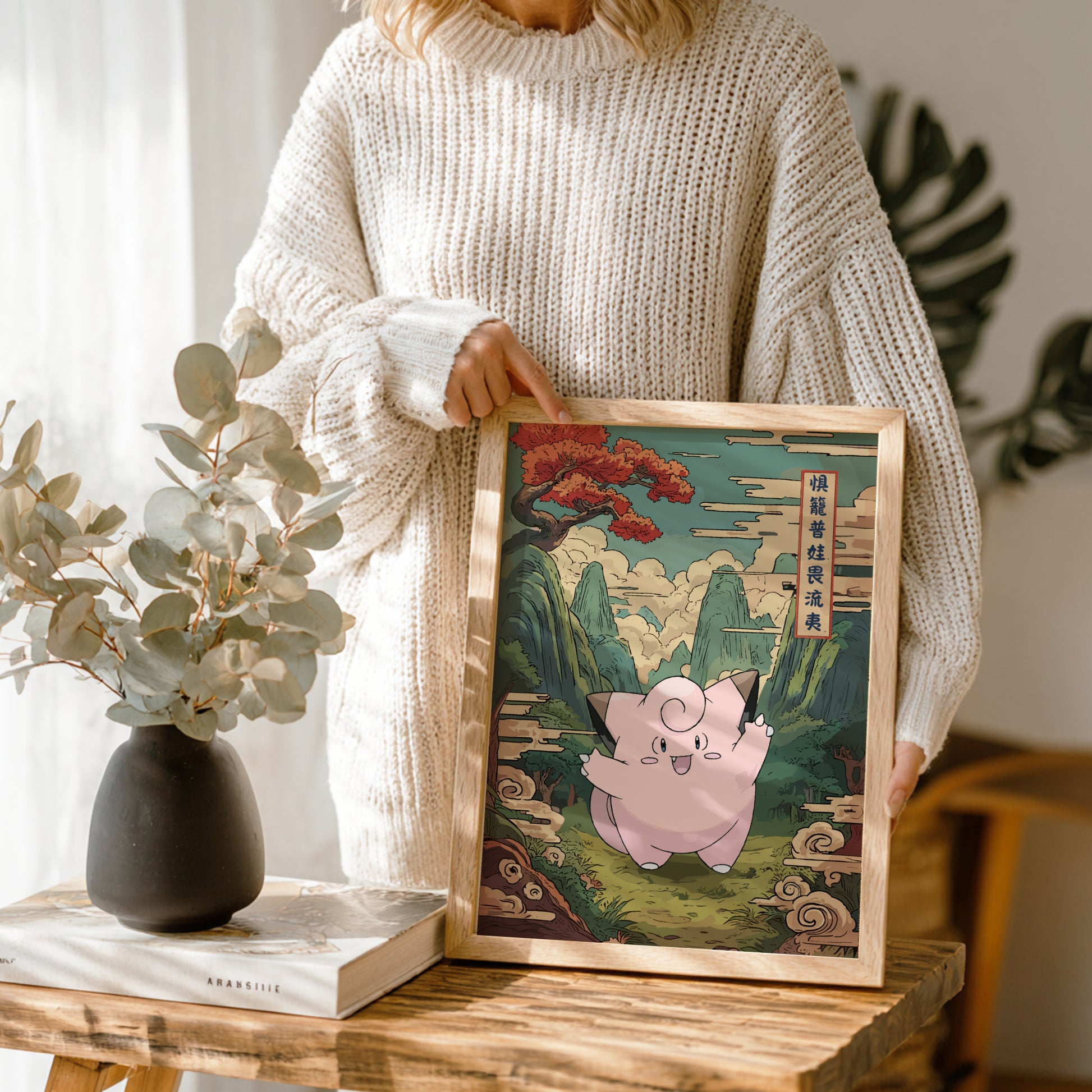 Person holding a framed artwork of Clefairy Pokemon character in a scenic setting