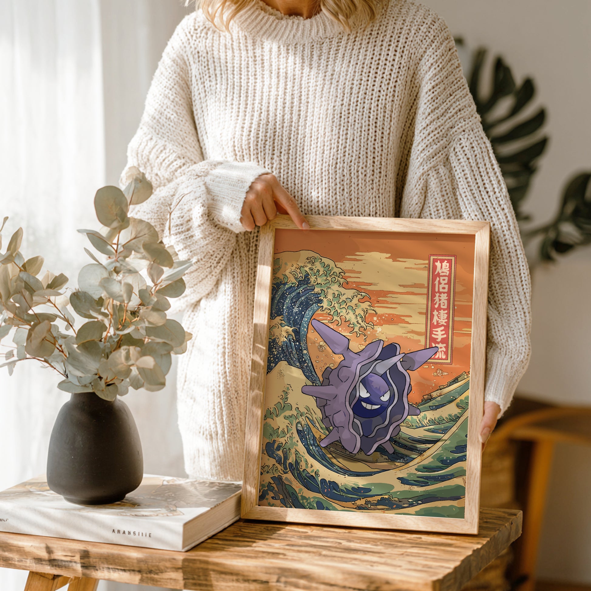 Person holding a framed artwork of a Cloyster Pokemon on a wave, similar to 'The Great Wave' by Hokusai, in a home setting.