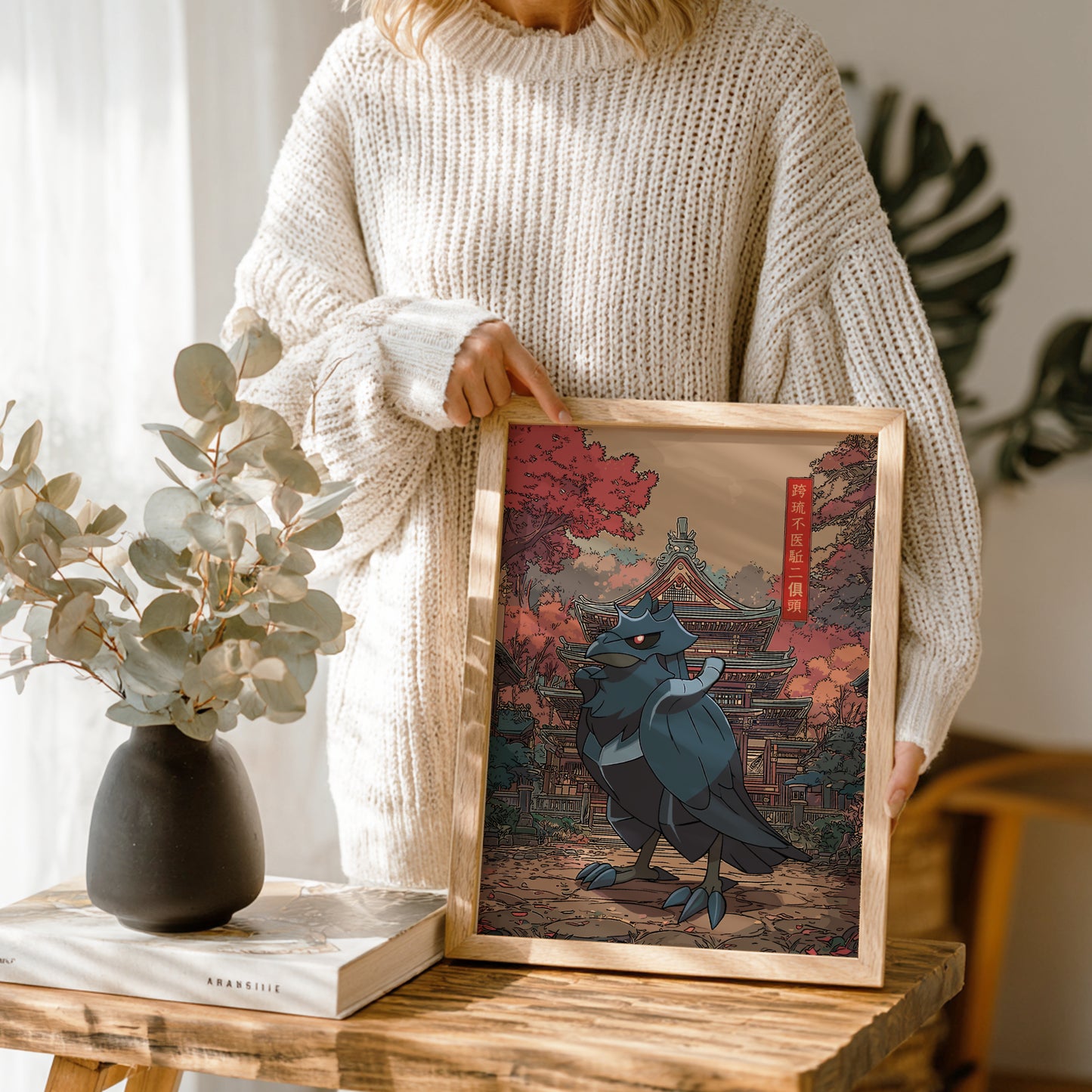 Person holding a framed artwork of Corviknight Pokemon in a traditional setting, with a vase and book on a wooden table.
