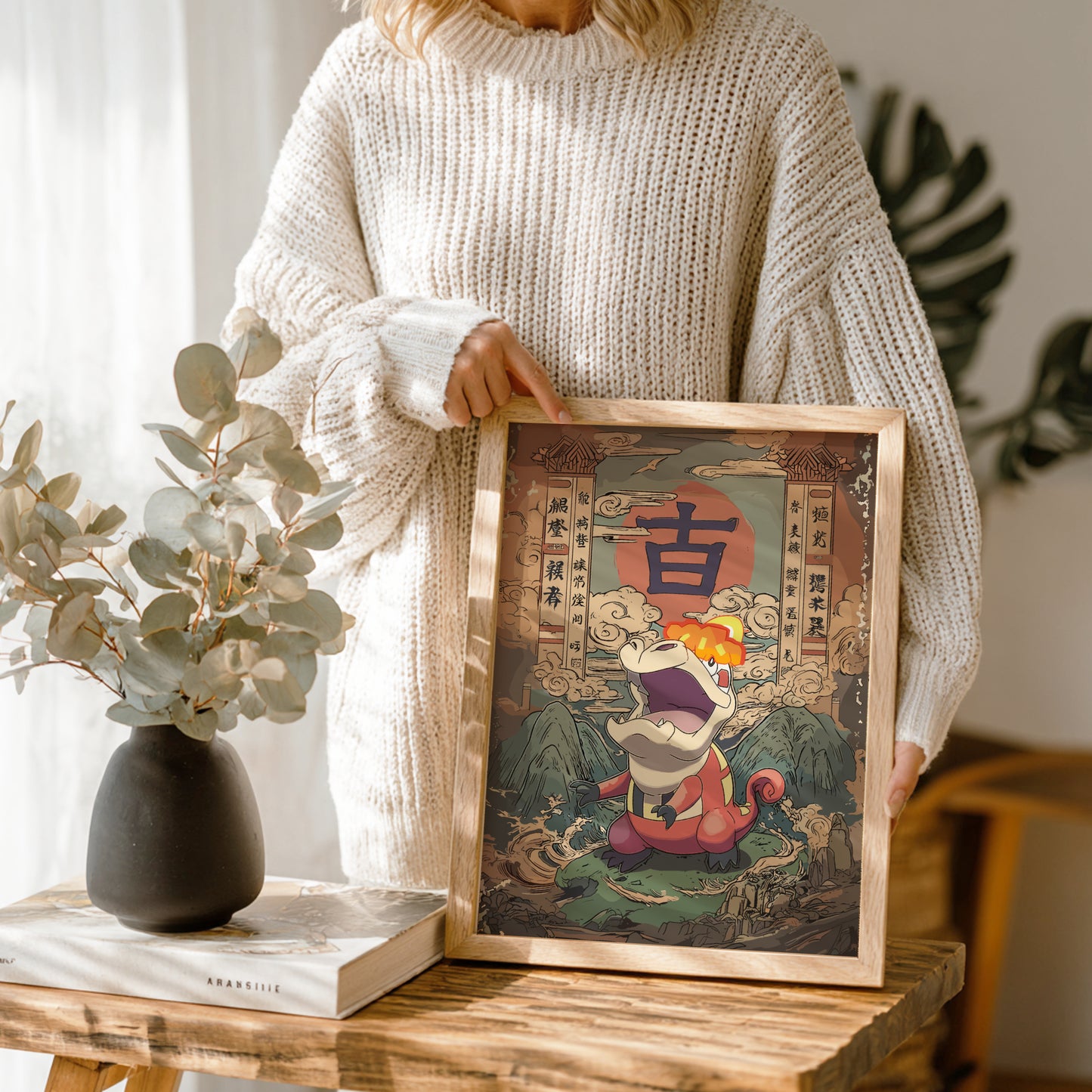 Person holding a framed artwork with a colorful design, standing in a room with plants and a vase.