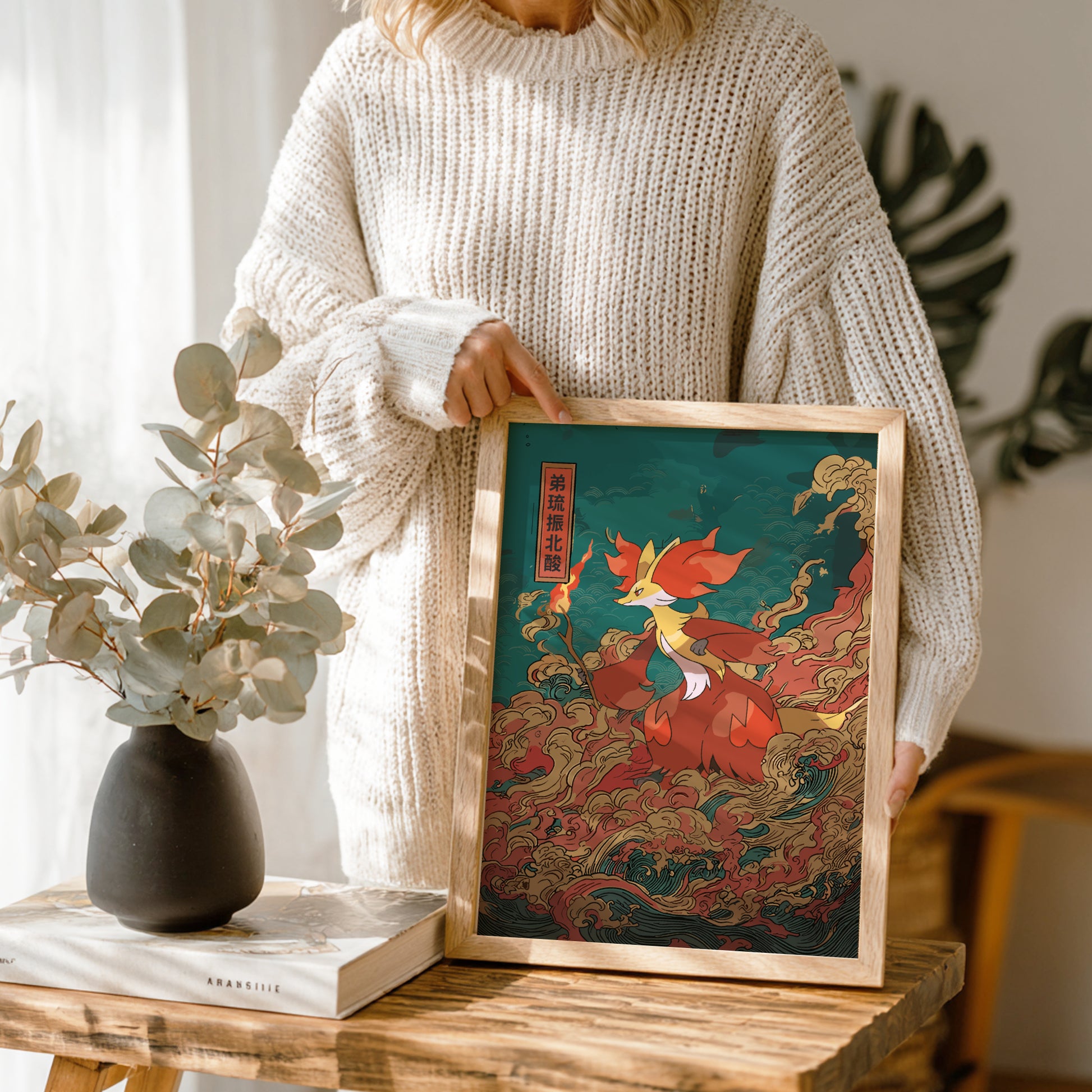 Person holding a framed artwork of Delphox Pokemon in a wooden frame on a wooden table.
