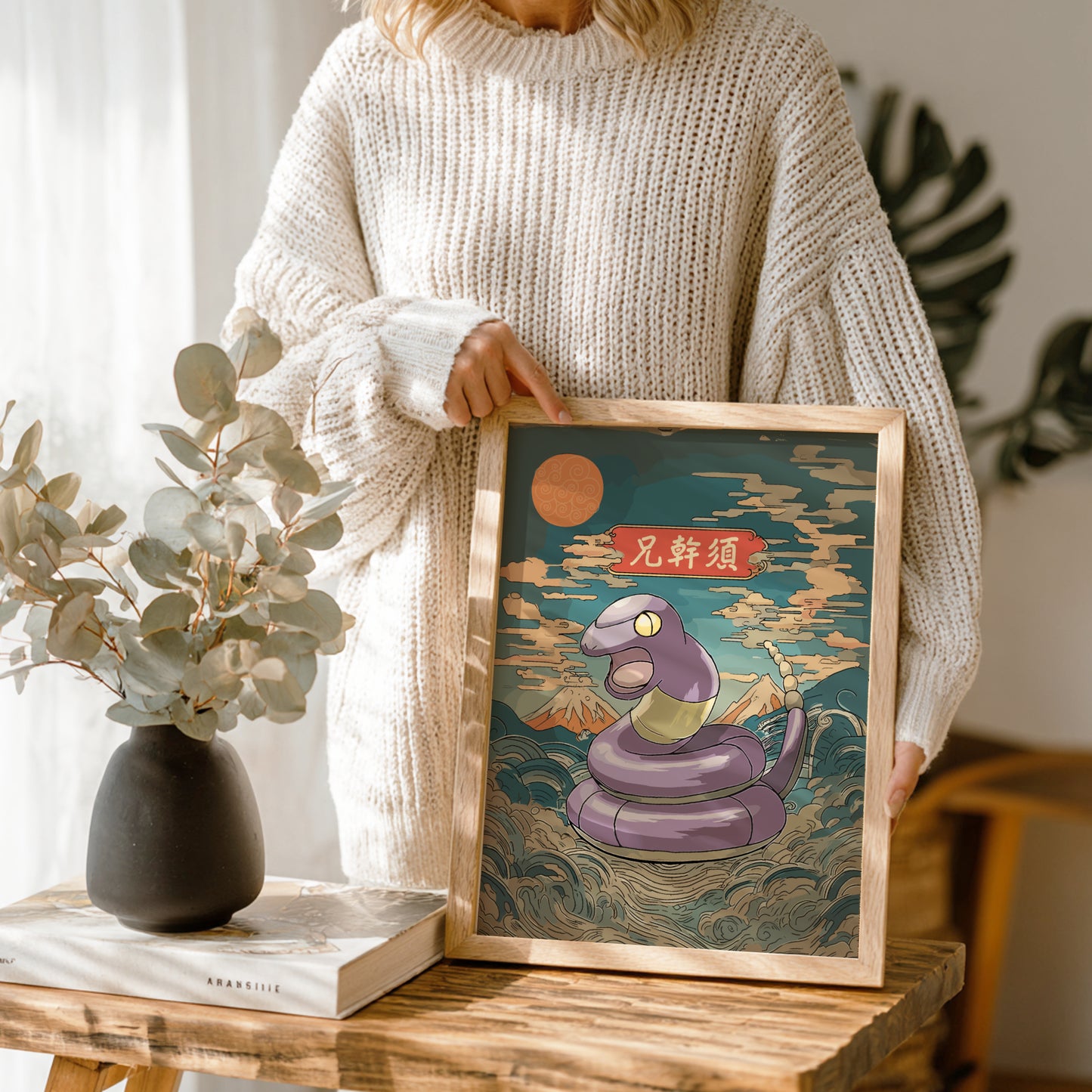 Person holding a framed artwork of Ekans Pokemon with a mountain and moon in the background.
