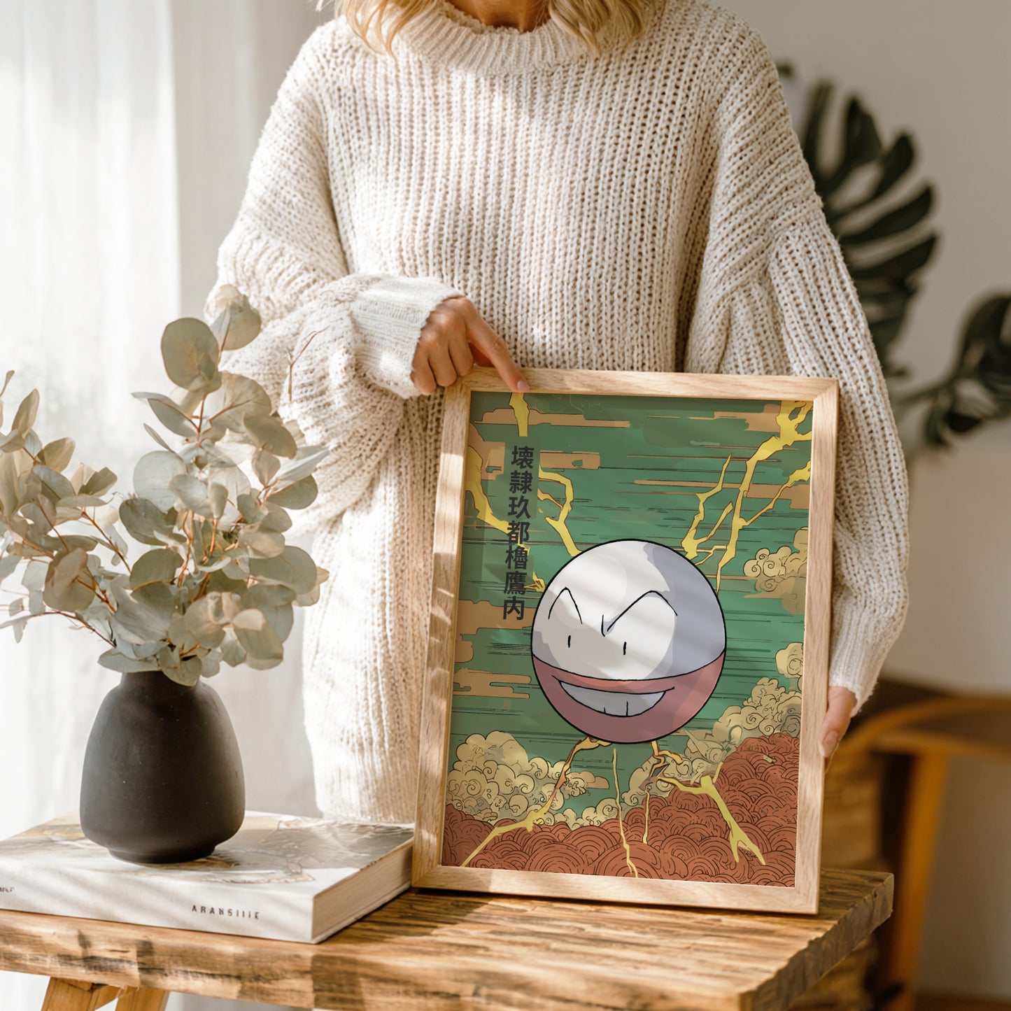 Person holding a framed illustration of a Electrode Pokemon character with a natural setting