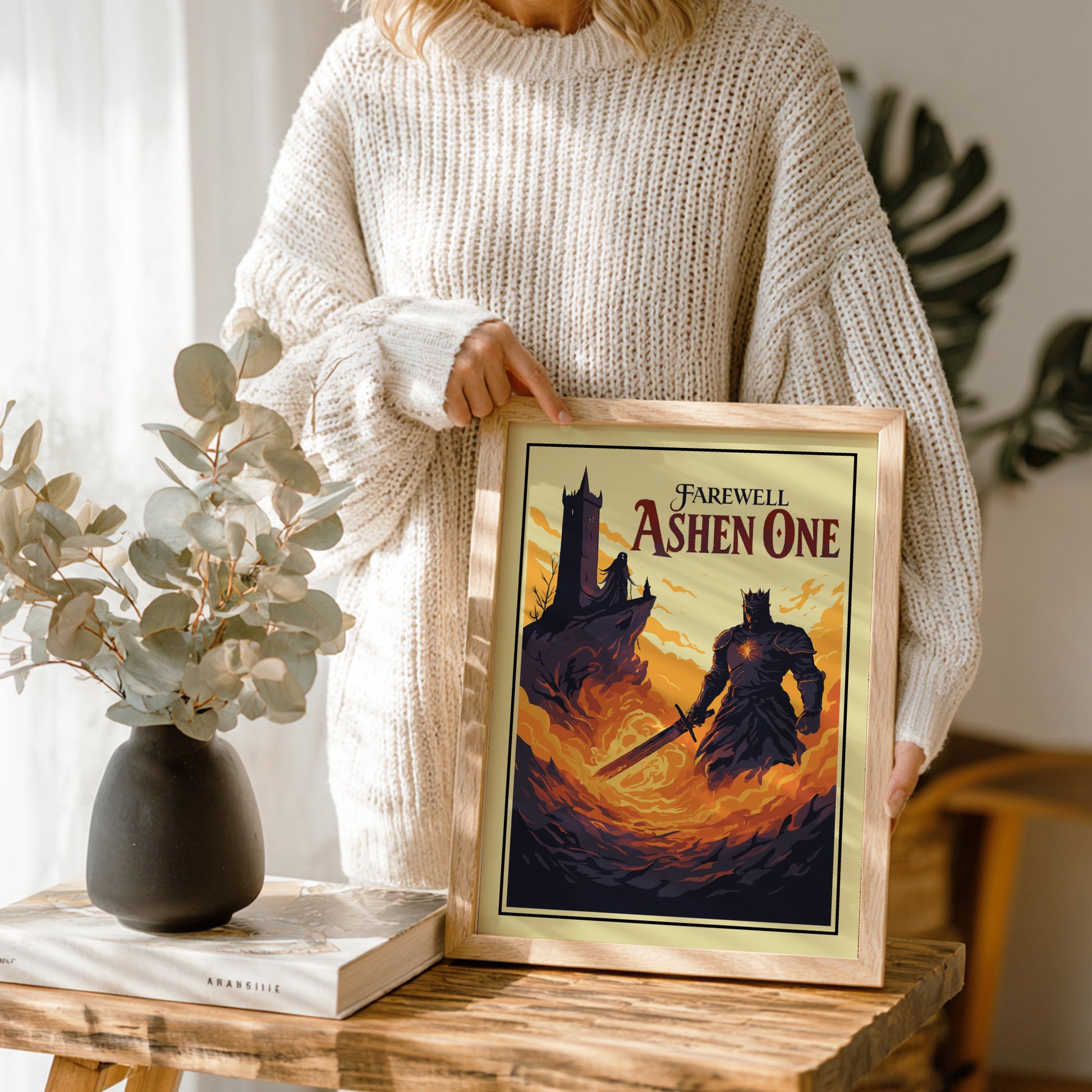 Person holding a framed artwork of Farewell Ashen One from Dark Souls on a wooden table.