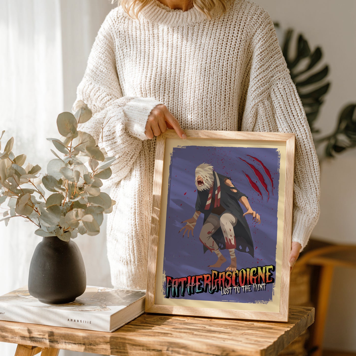Person holding a framed artwork of Father Gascoigne from Bloodborne on a wooden table.
