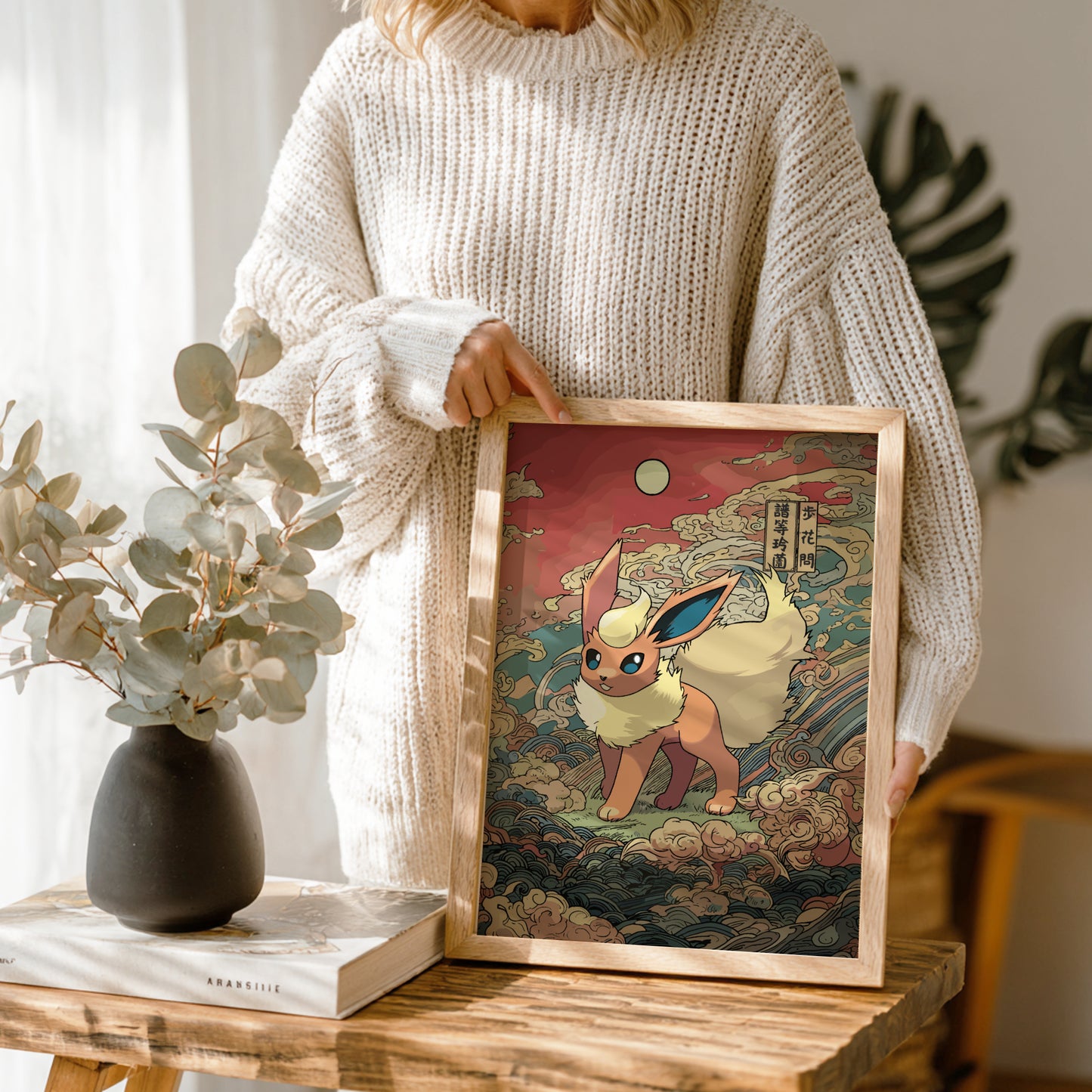 Person holding a framed artwork of Flareon Pokemon character in a room with plants and decor.