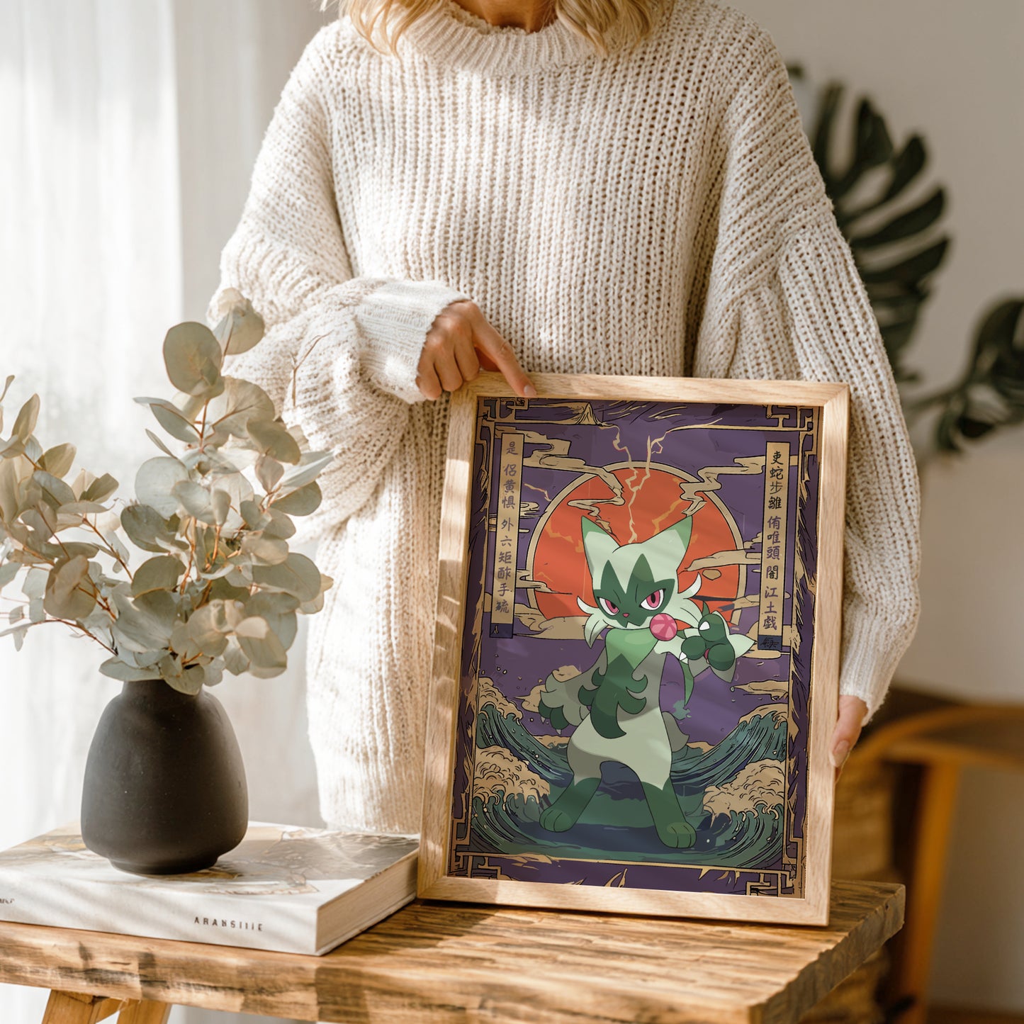 Person holding a framed artwork of Floragato Pokemon with a red background, standing next to a vase and book on a wooden table.
