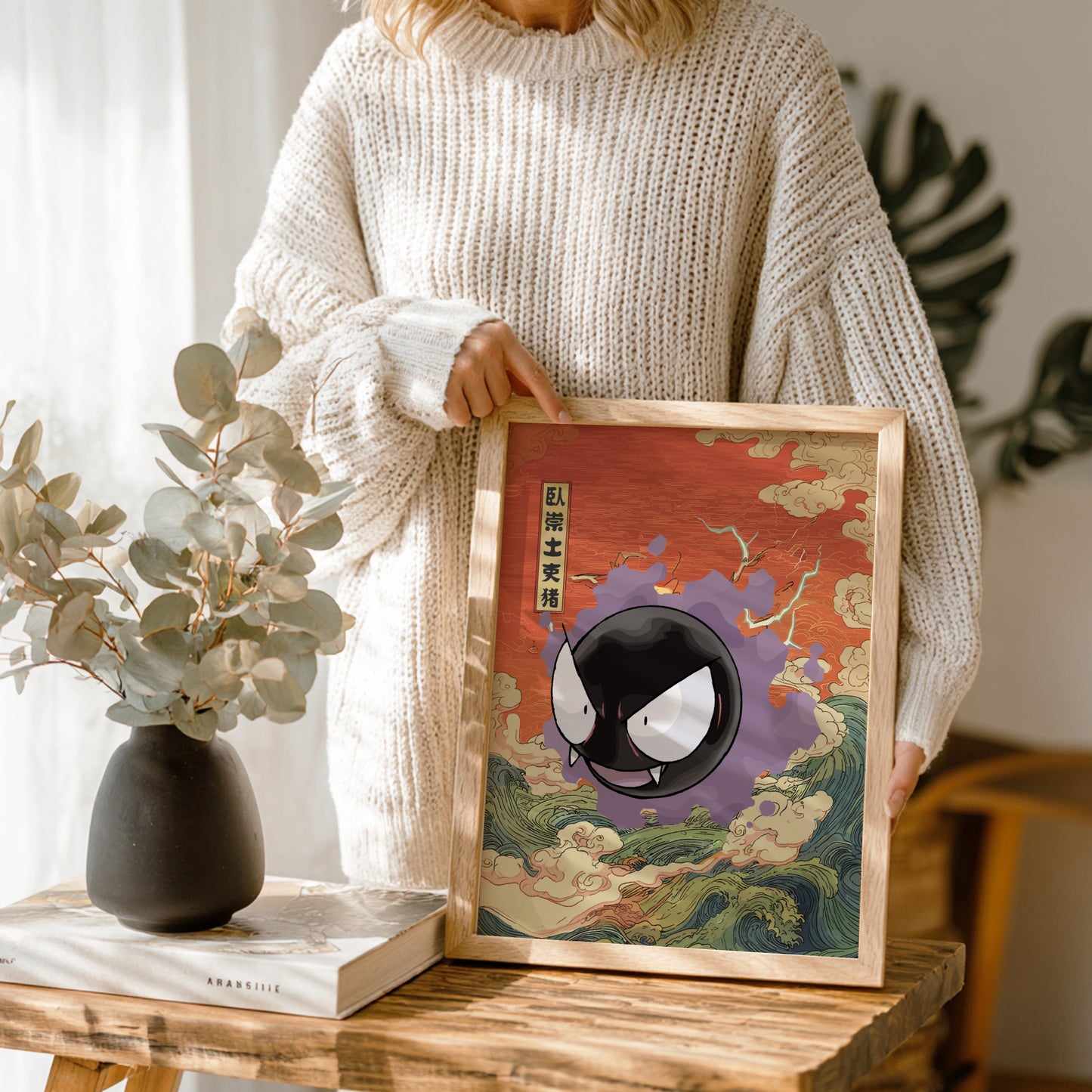 Person holding a framed artwork with a stylized Gastly Pokemon in a decorative setting