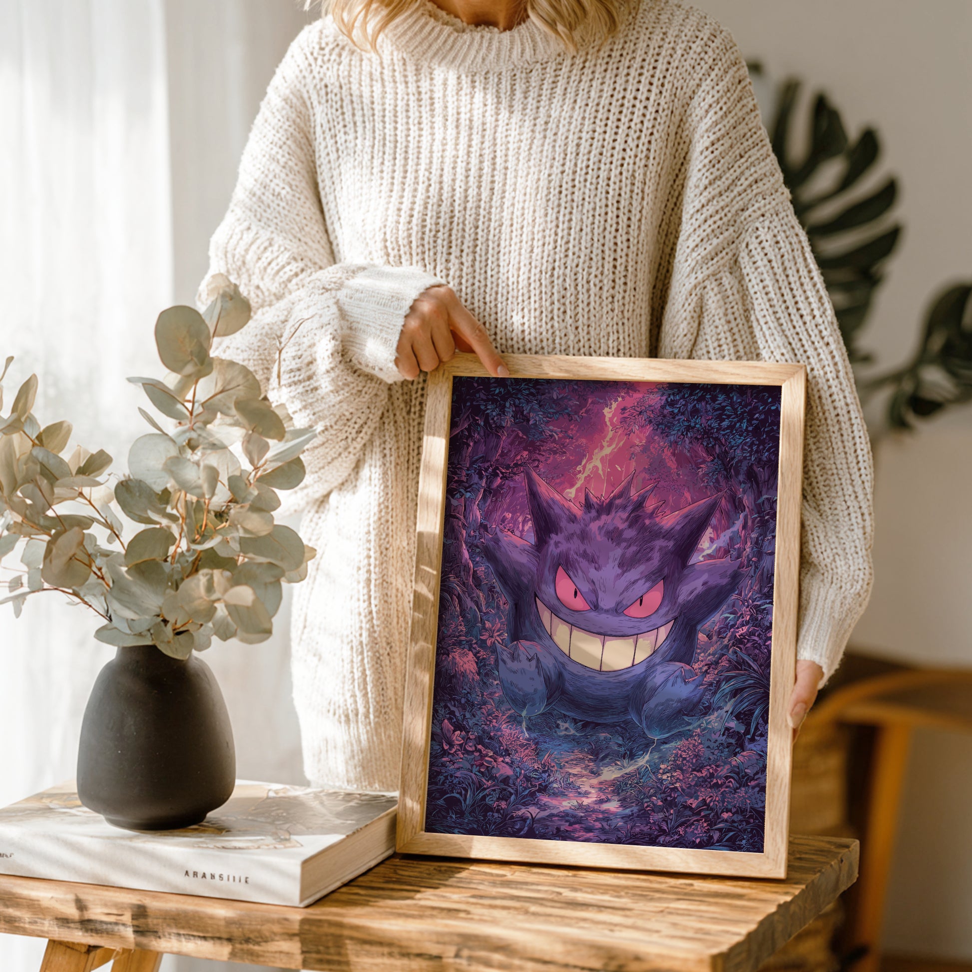 Person holding a framed artwork of Gengar Pokemon on a wooden table.