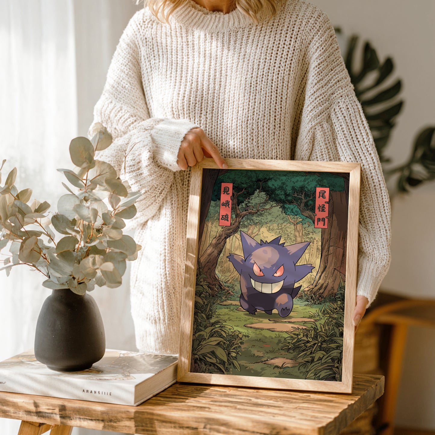 Person holding a framed artwork of a stylized Gengar Pokémon in a natural setting