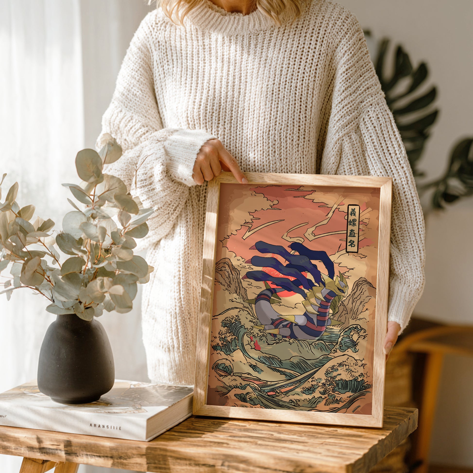 Person holding a framed artwork with Giratina Pokemon design in a home setting