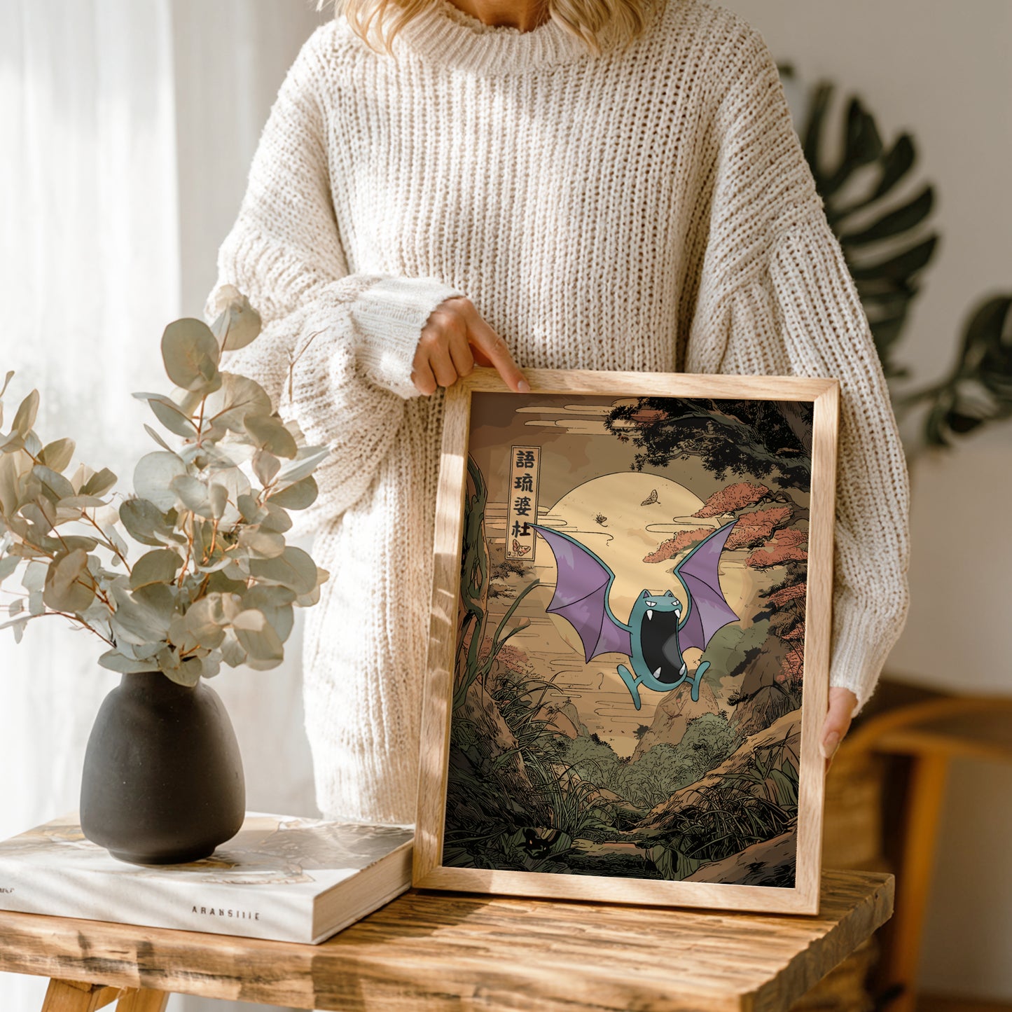 Person holding a framed artwork with Golbat Pokemon design in a cozy indoor setting.