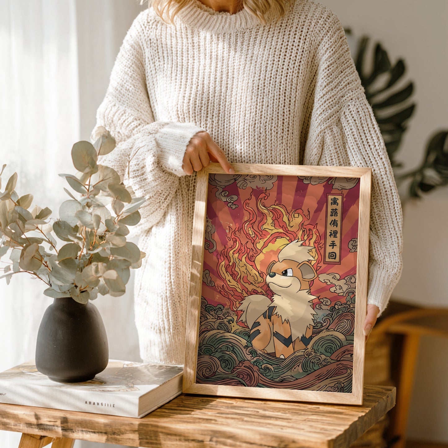 Person holding a framed artwork of Growlite Pokemon with flames, in a cozy indoor setting.