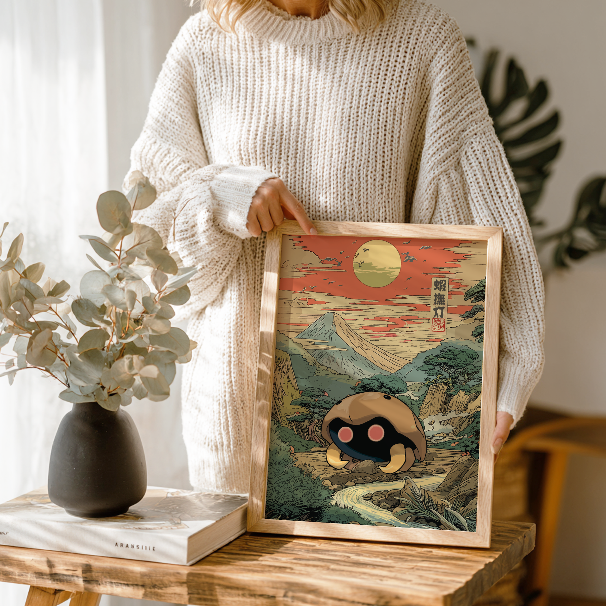 Person holding a framed artwork of a mountain landscape with Kabuto Pokemon in a wooden frame.