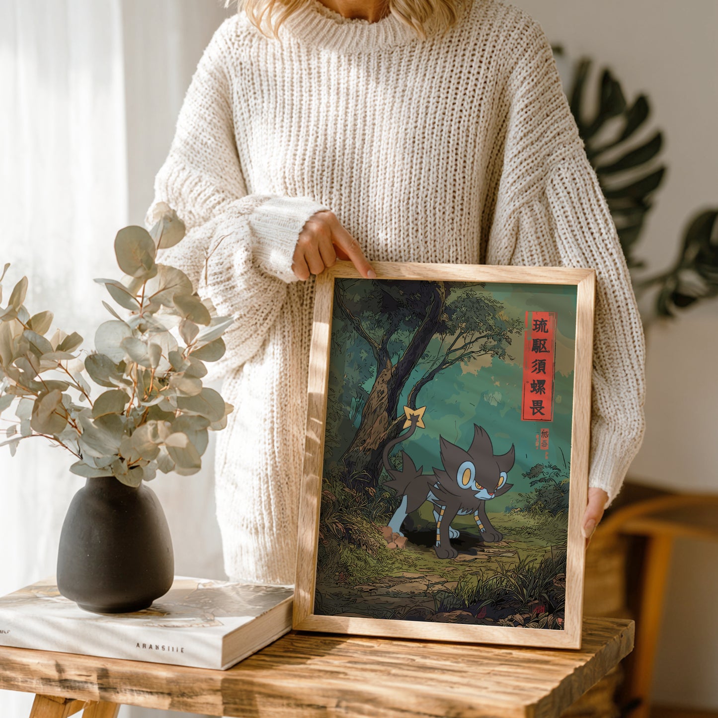 Person holding a framed artwork of Luxray Pokemon character in a forest setting, with a vase and book on a table in the foreground.