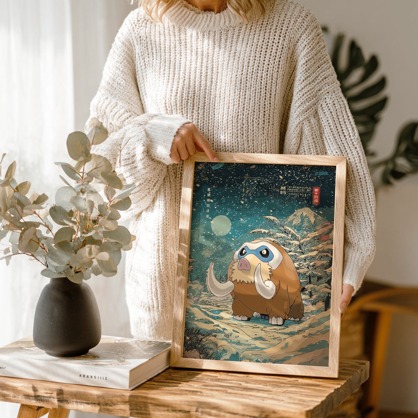Person holding a framed illustration of Mamoswine Pokemon character in a scenic setting