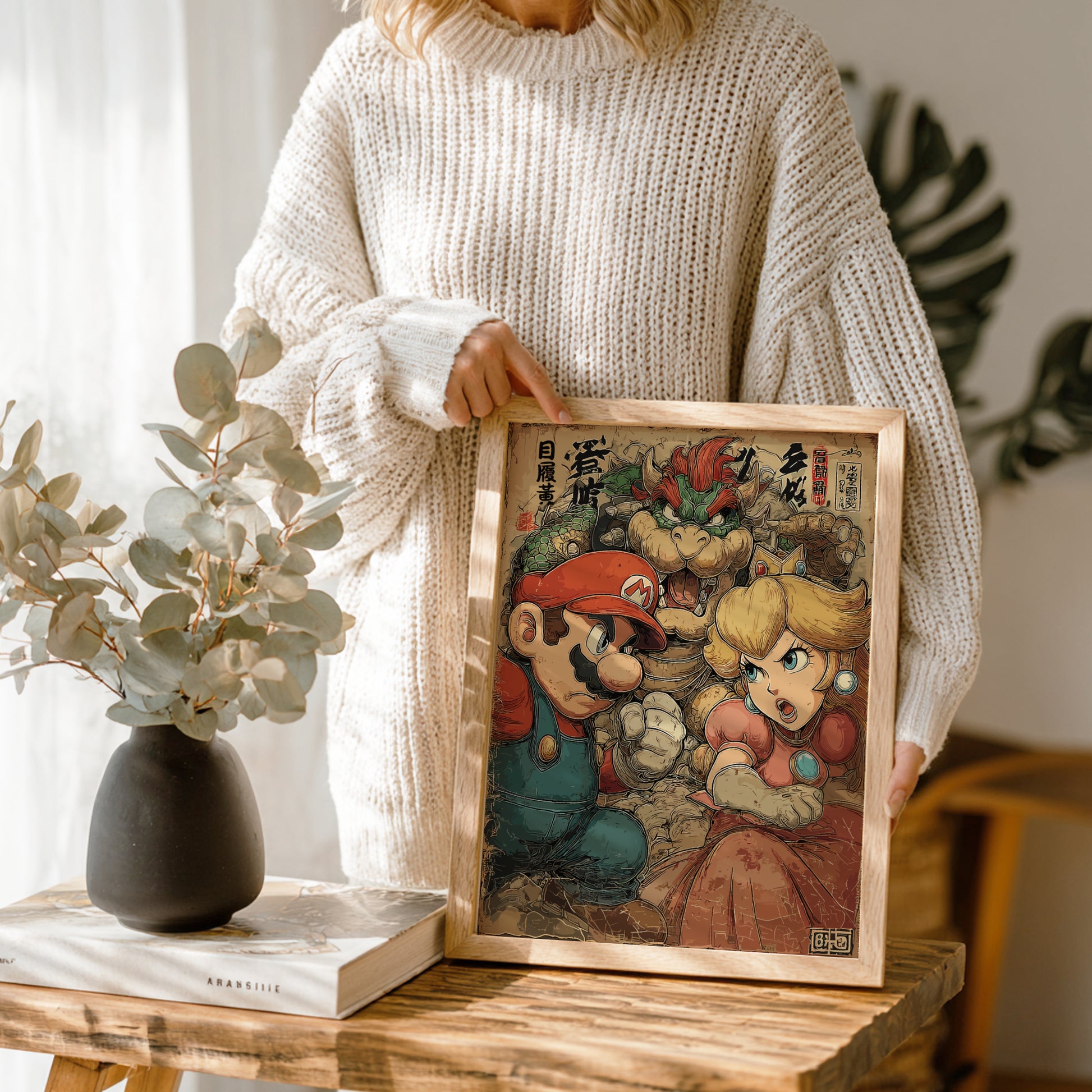 Person holding a framed artwork of Mario, Bowser and Princess Peach characters on a wooden table.