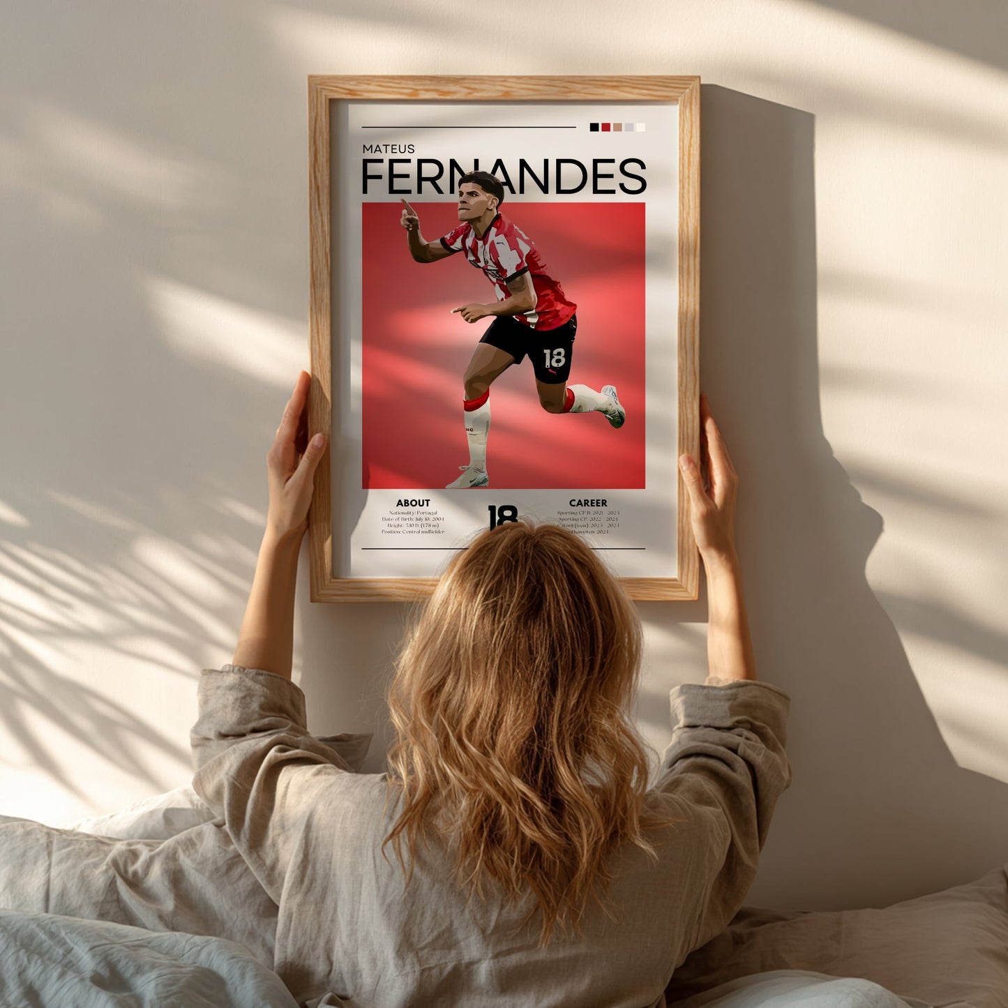 Person hanging a framed poster of a soccer player named Fernandes on a wall.