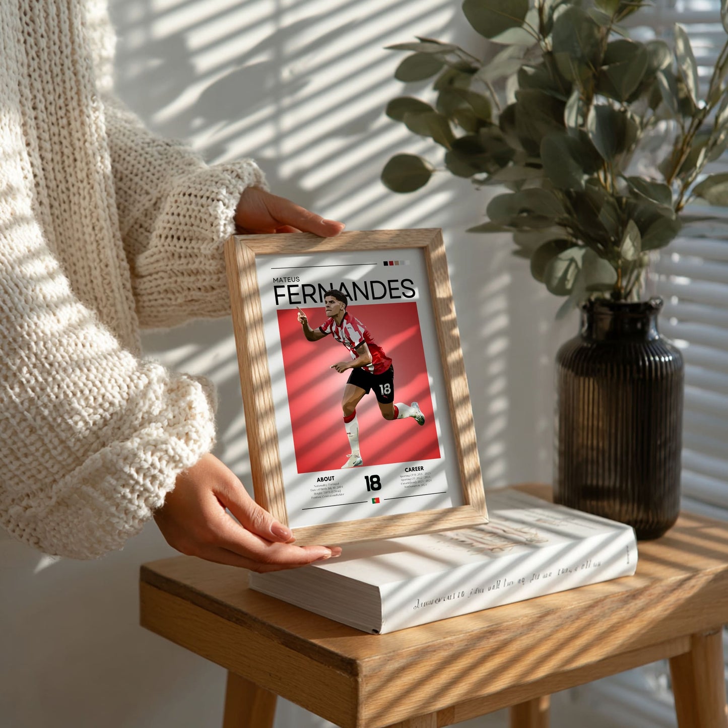 Person holding a framed picture of a soccer player on a wooden table with a plant in the background