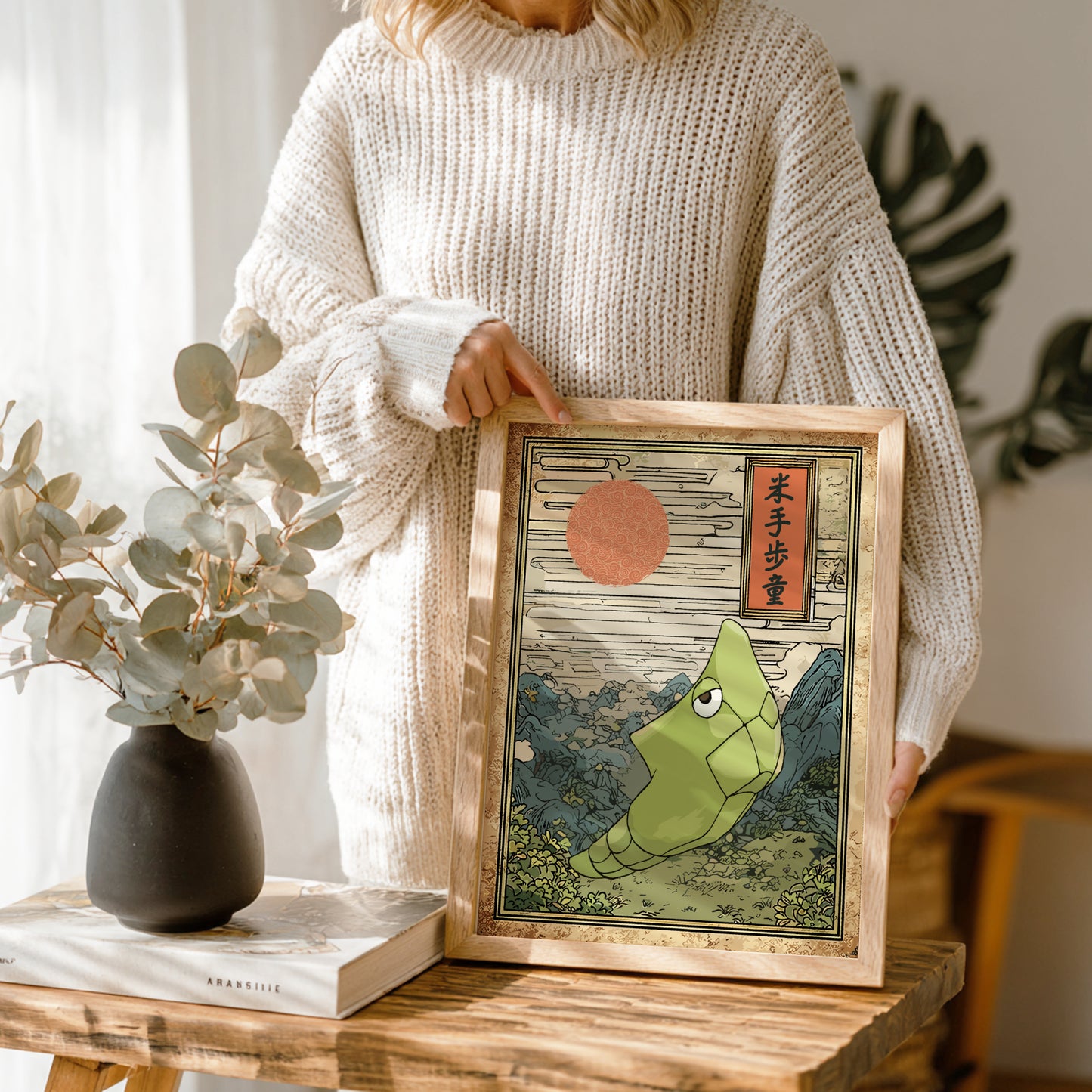 Person holding a framed artwork of Metapod Pokemon with a red sun in a wooden frame.