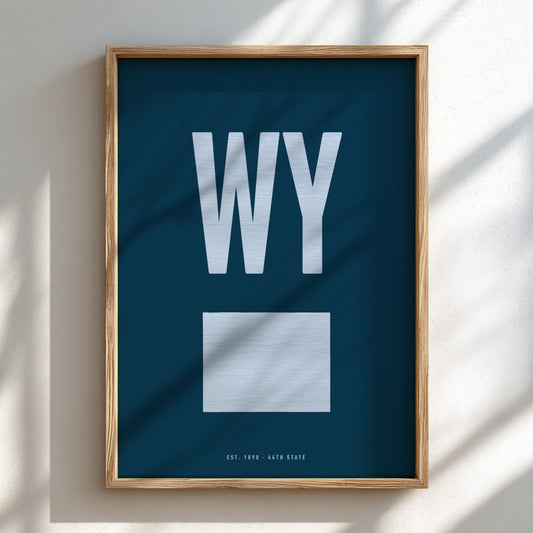 Framed poster with 'WY' on a blue background, leaning against a light wall.