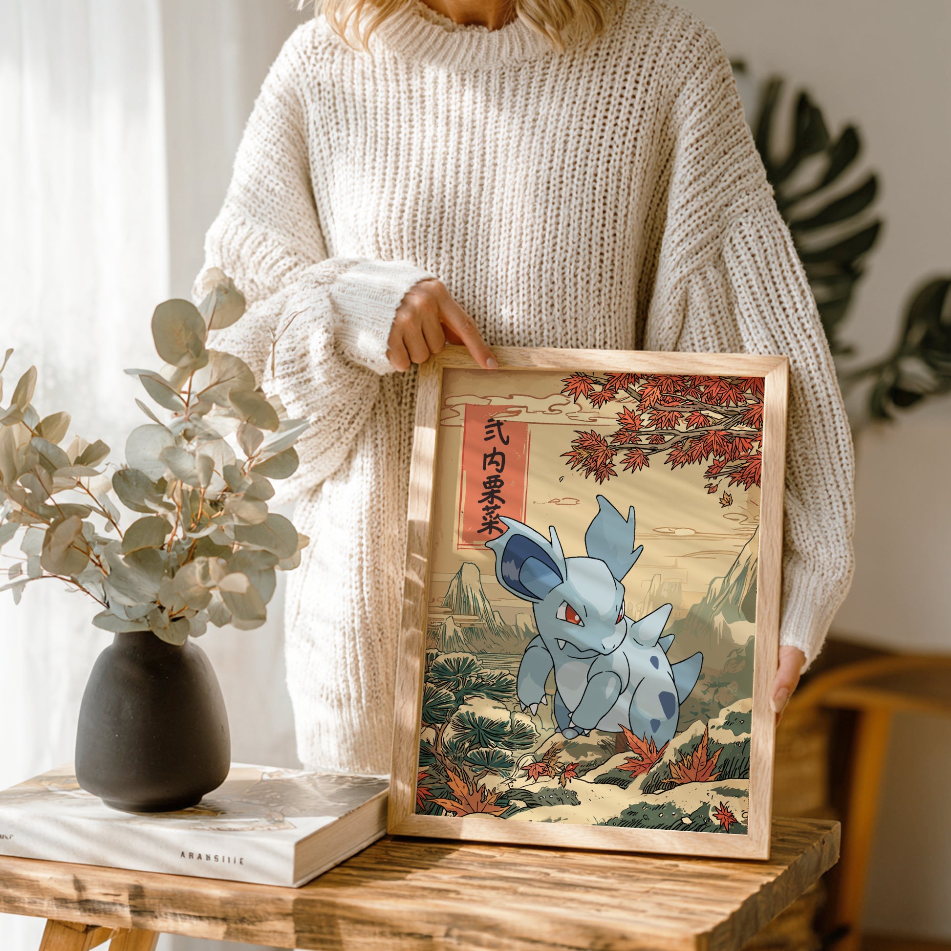 Person holding a framed artwork of Nidorina Pokemon in a scenic setting