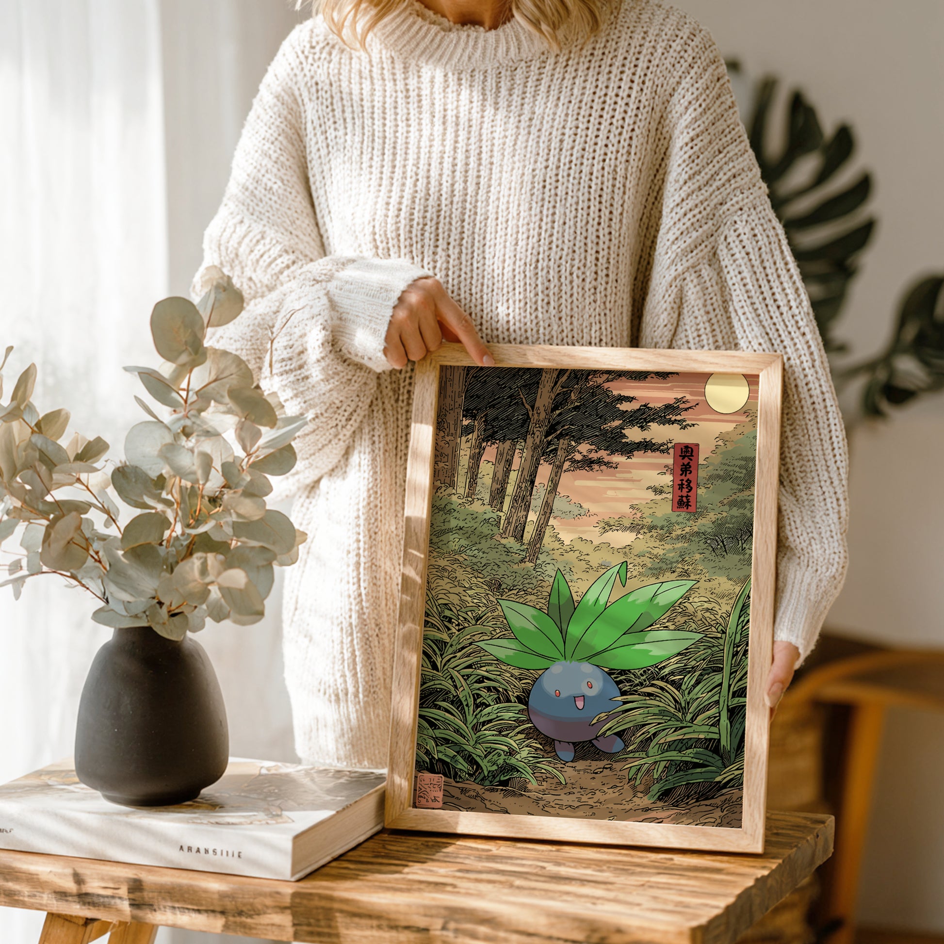 Person holding a framed illustration of Oddish Pokémon in a forest setting.