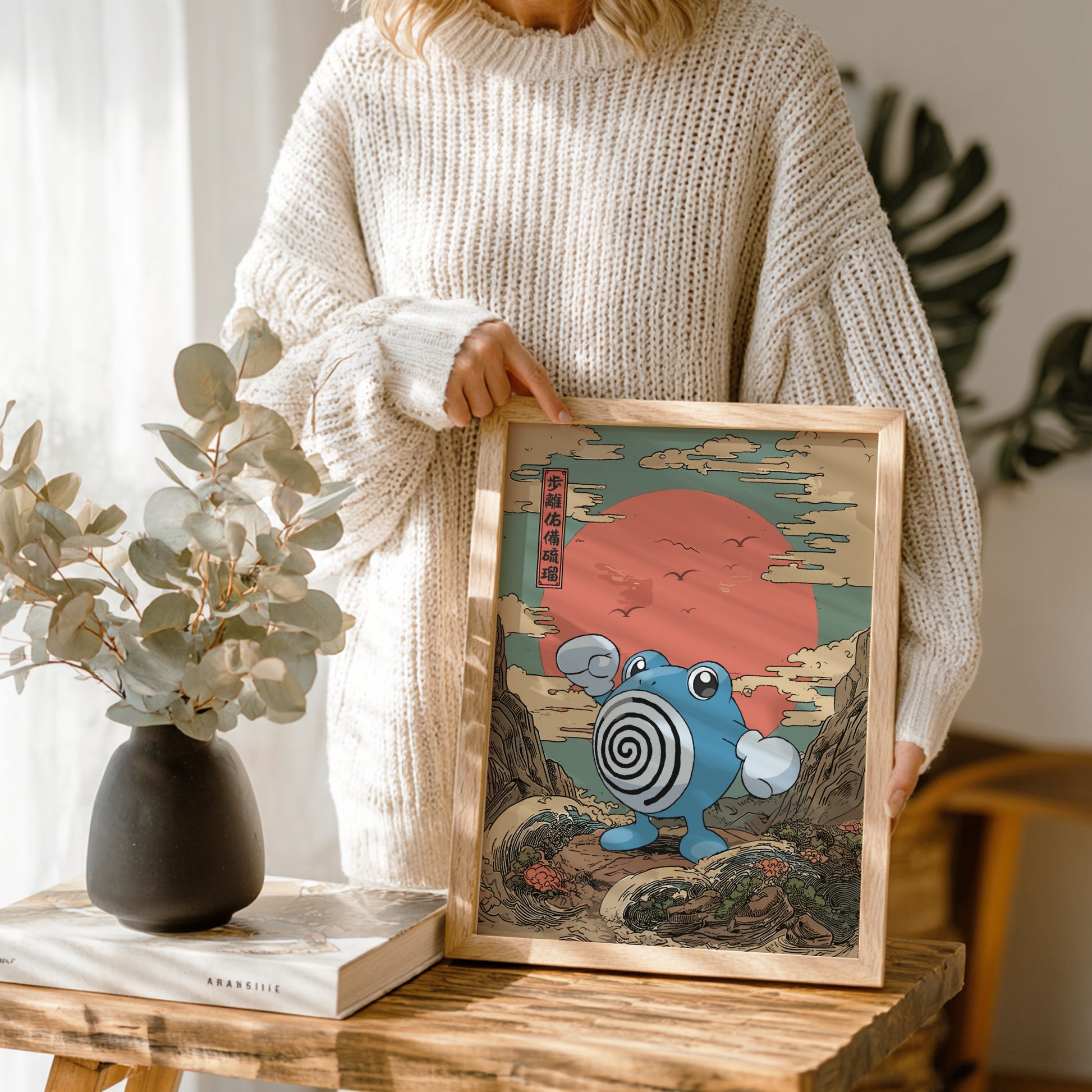 Person holding a framed artwork with Poliwhirl Pokemon and Japanese text, standing in a room with plants and decor.