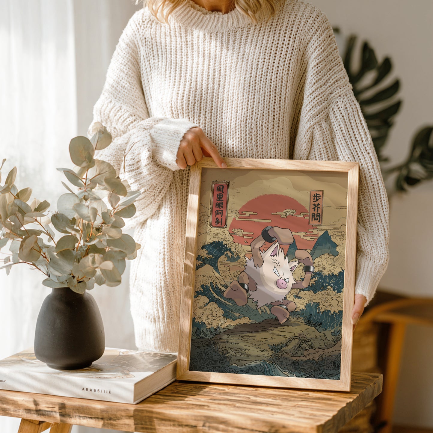 Person holding a framed artwork of a traditional Japanese print on a wooden table.