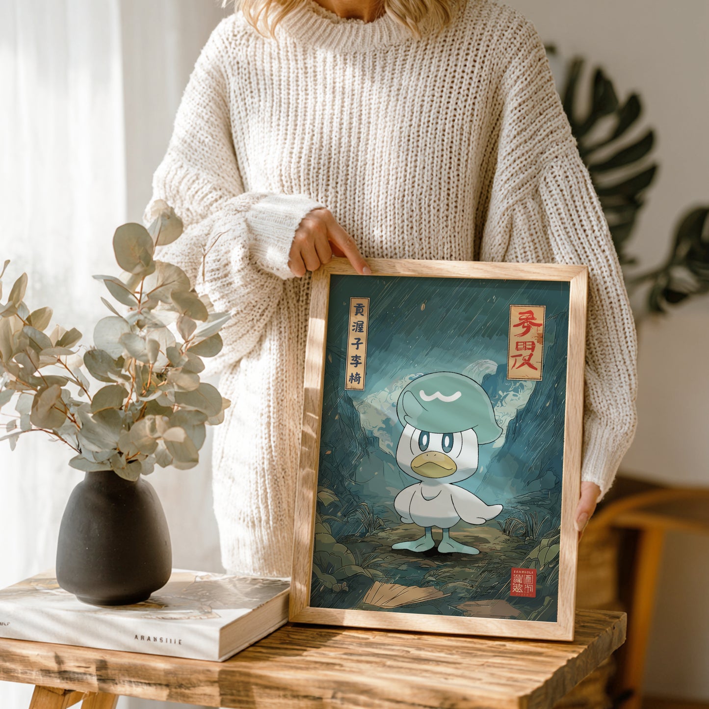 Person holding a framed illustration of Quaxly Pokemon character in a room with plants and decor.