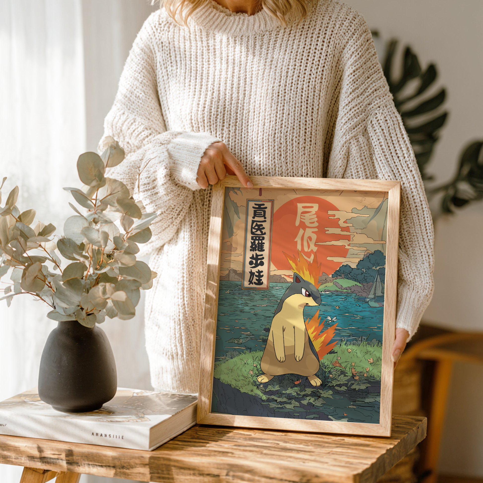 Person holding a framed artwork of a stylized Quilava Pokemon by a window with plants.