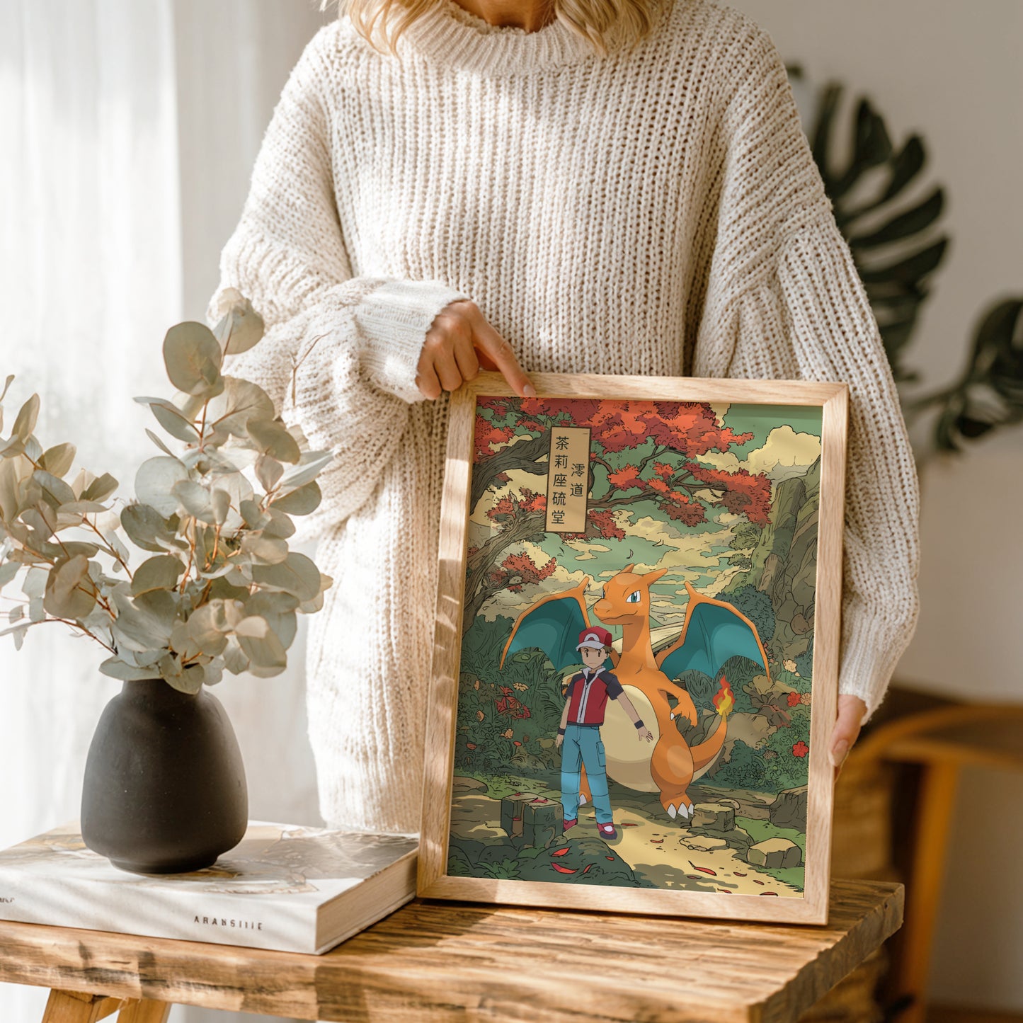 Person holding a framed illustration of Red and Charizard Pokemon on a wooden table.