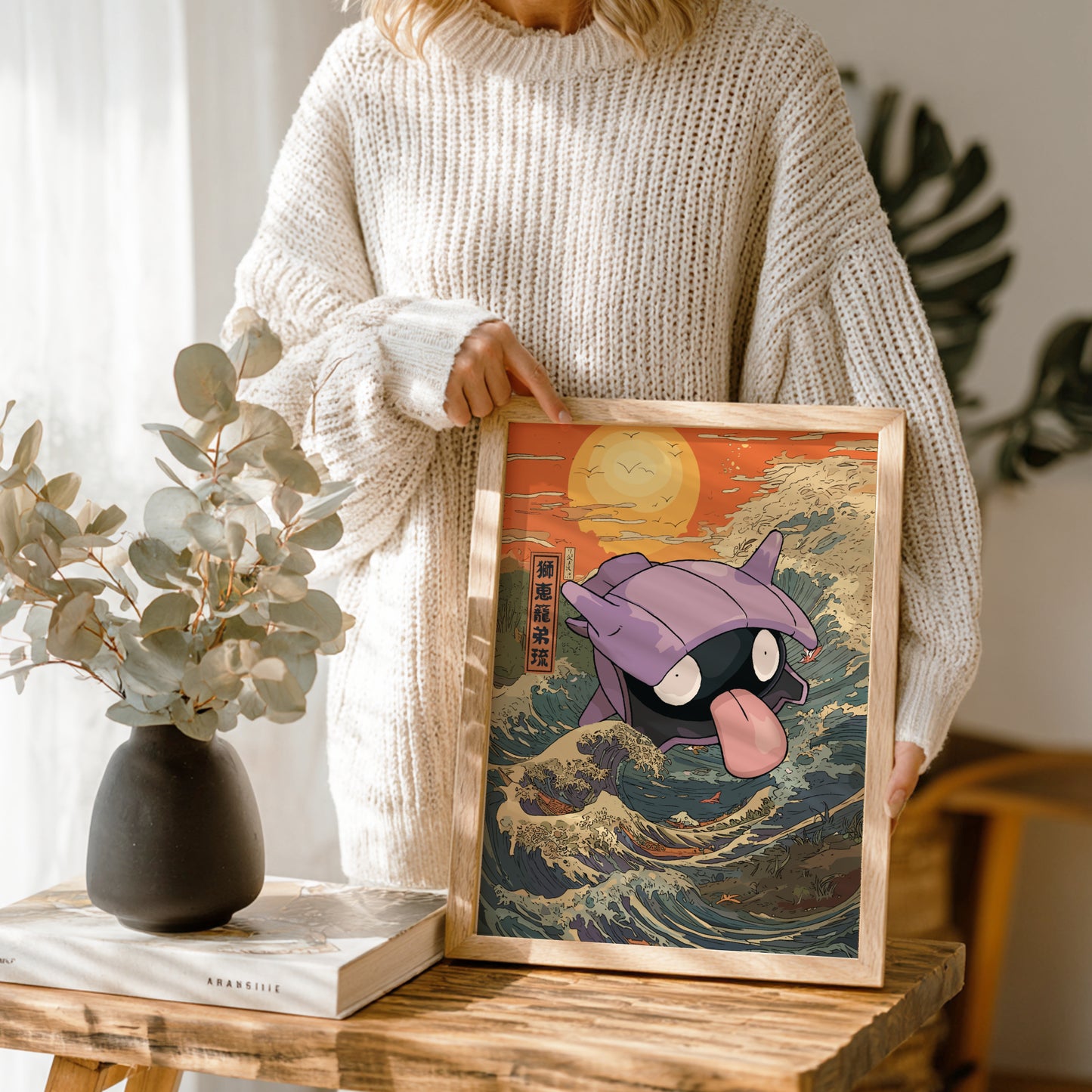 Person holding a framed artwork of Shellder Pokemon on a wooden table with plants in the background