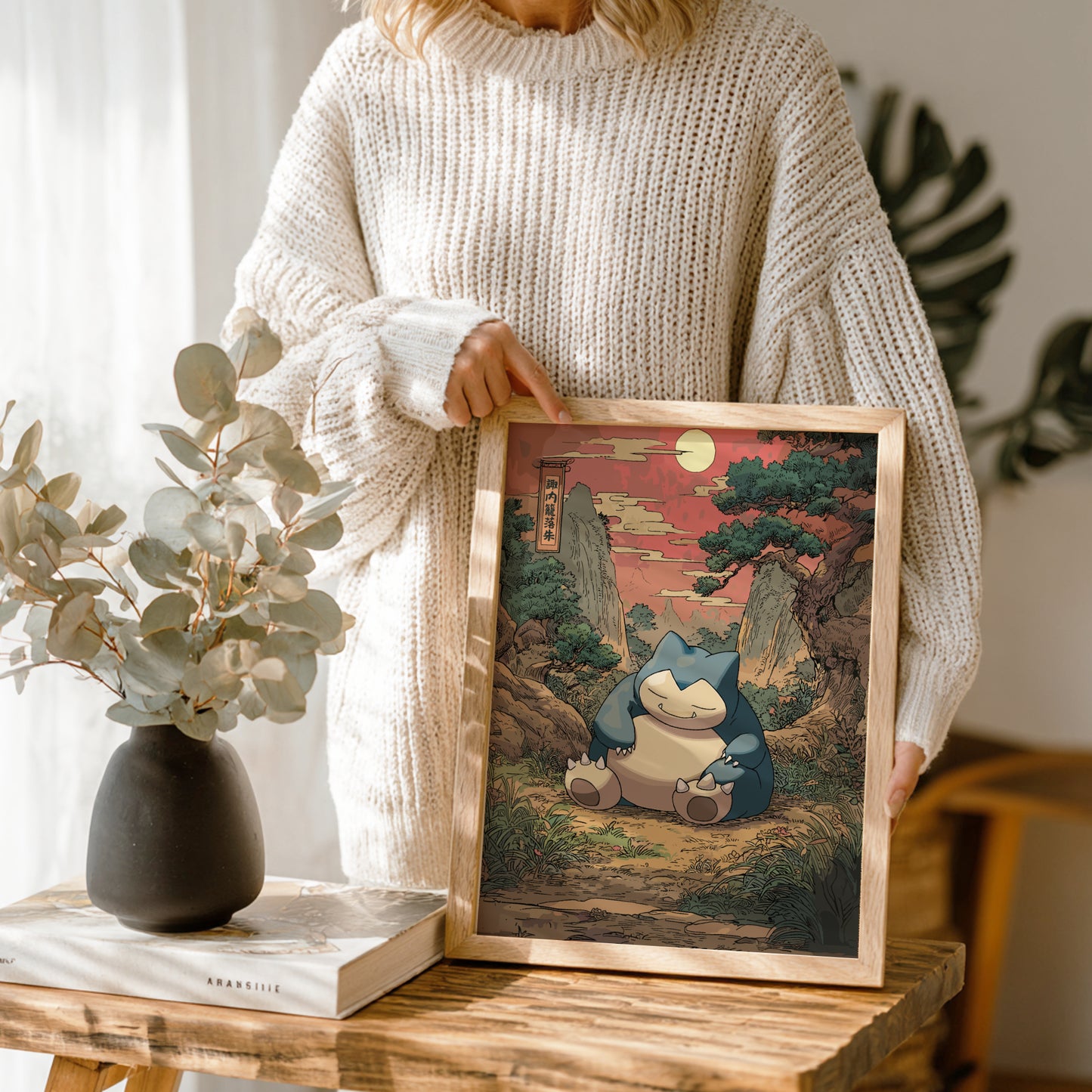 Person holding a framed artwork of Snorlax Pokemon character in a natural setting