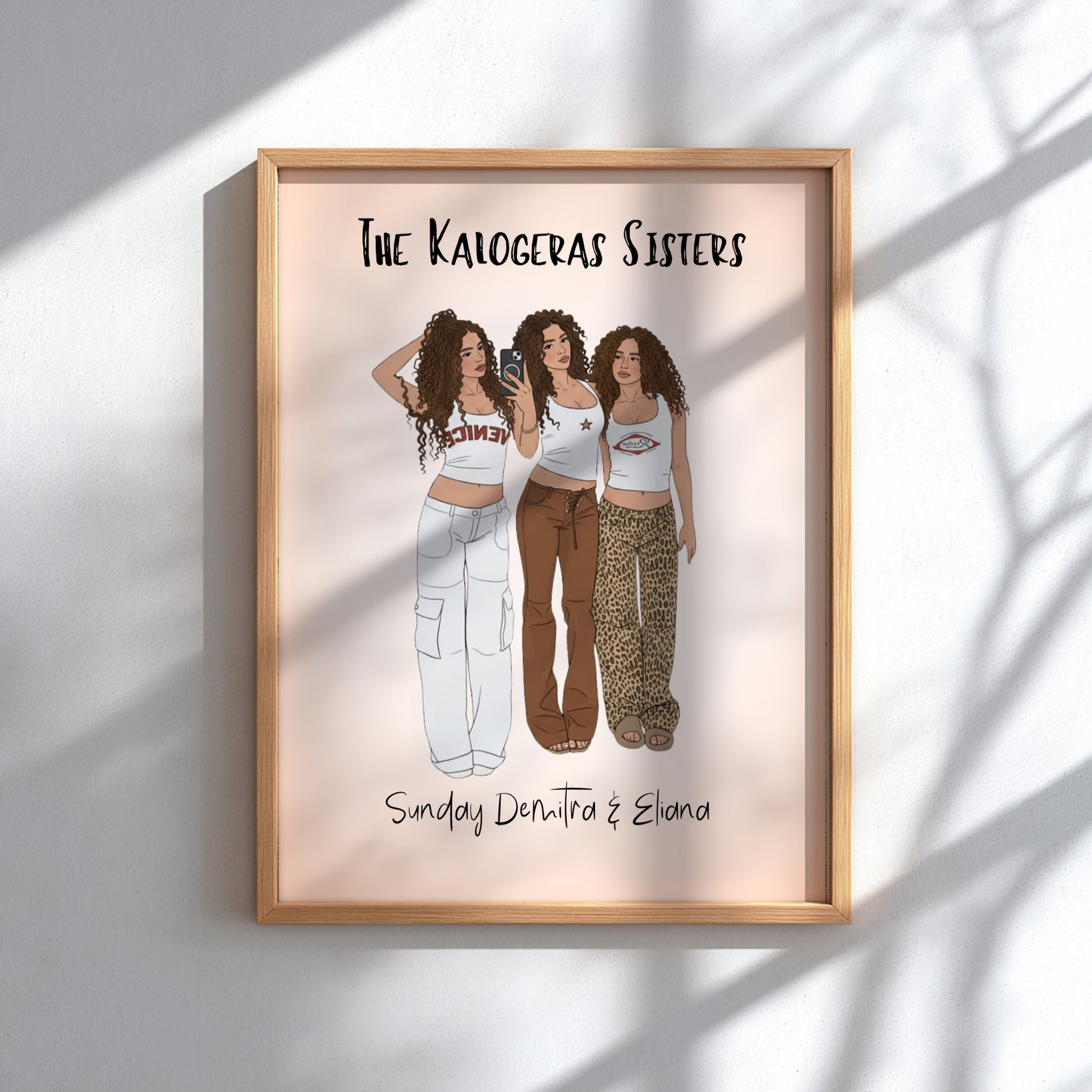 Framed artwork of 'The Kalogeras Sisters' with three illustrated women in different outfits.