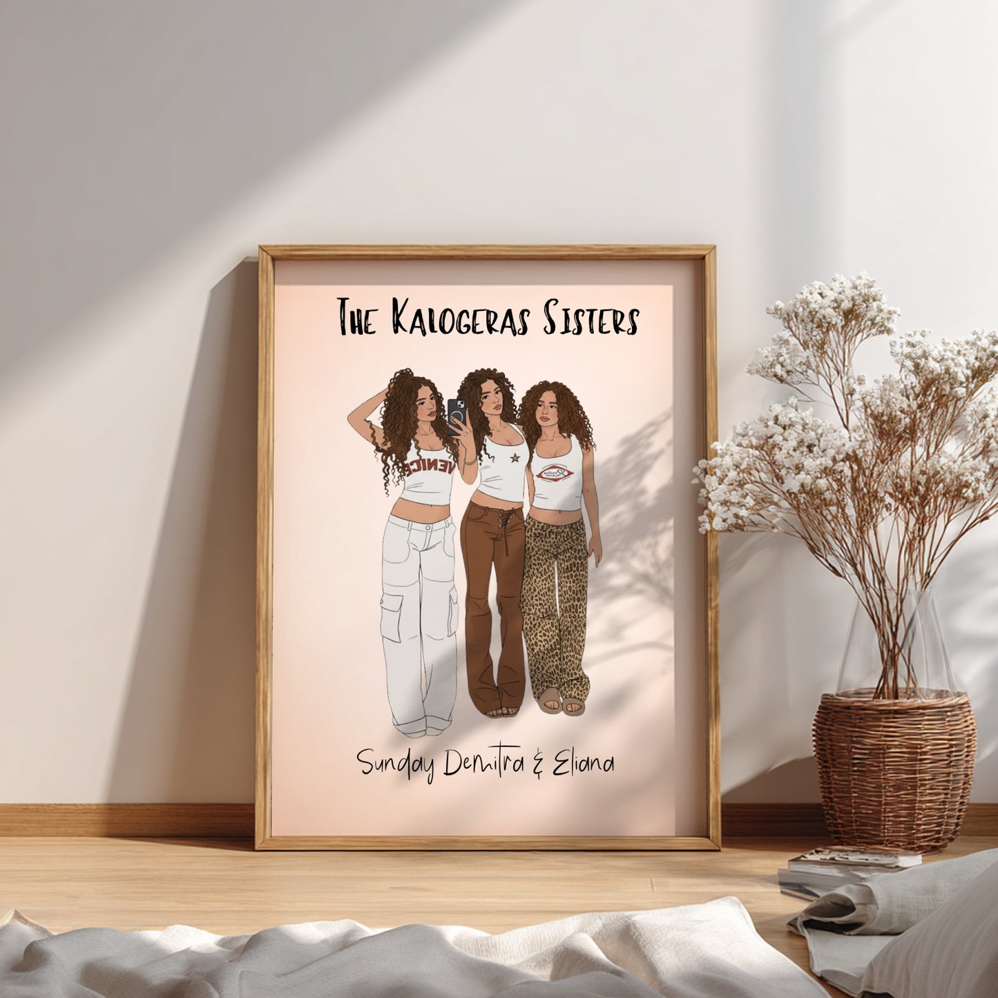 Framed artwork of 'The Kaliogeras Sisters' on a wall with a plant and decor items.