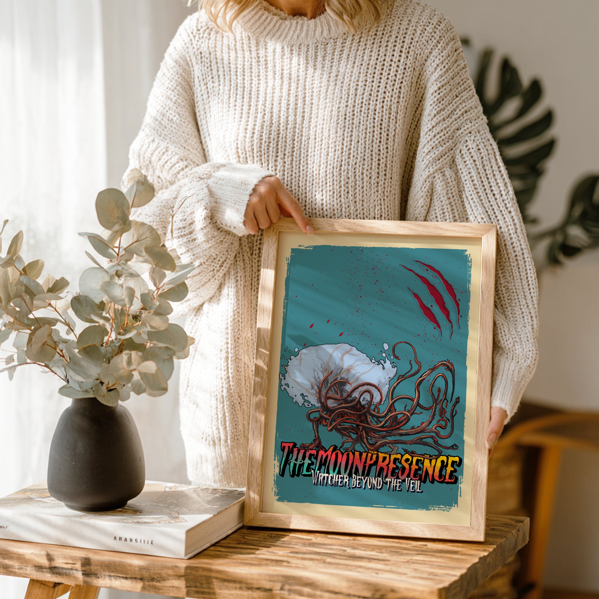 Person holding a framed artwork of The Moon Presence from Bloodborne on a wooden table.