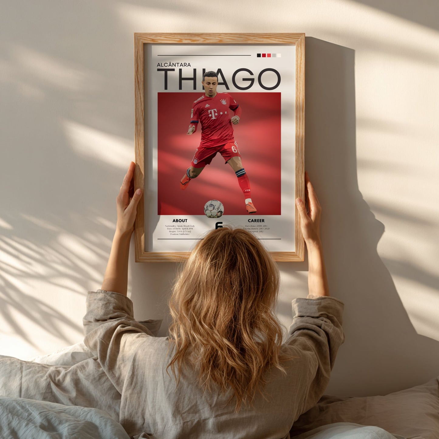 Person hanging a framed poster of a soccer player named Thañgo on a wall.