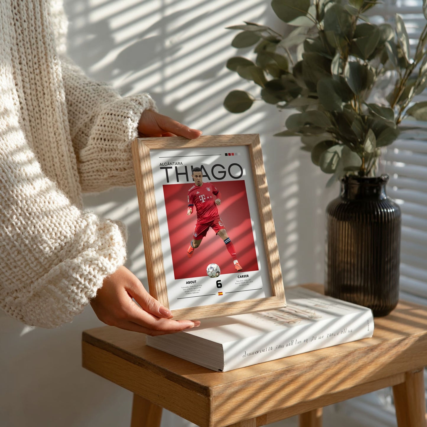 Person holding a framed picture of a person in a red outfit on a wooden table with a plant in the background.