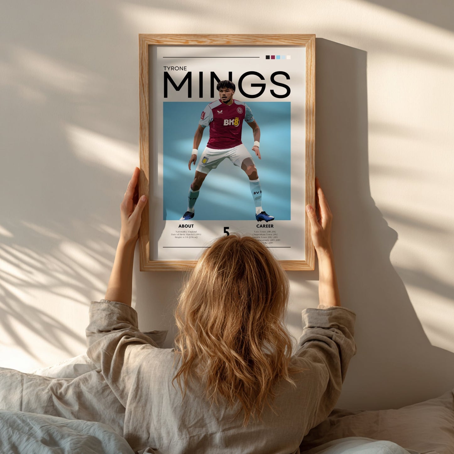 Person hanging a framed poster of a soccer player named Mings on a wall.