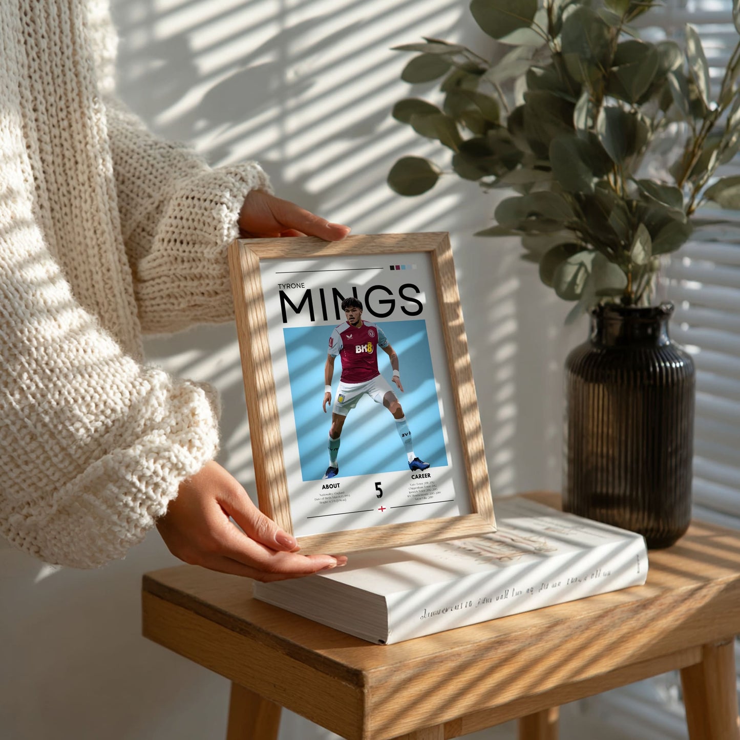 Person holding a framed picture of a sports player on a wooden table with a plant in the background