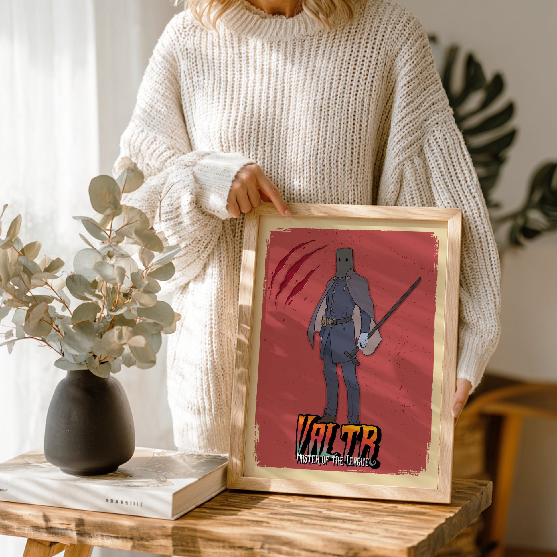 Person holding a framed artwork of Valtr from Bloodborne on a wooden table.